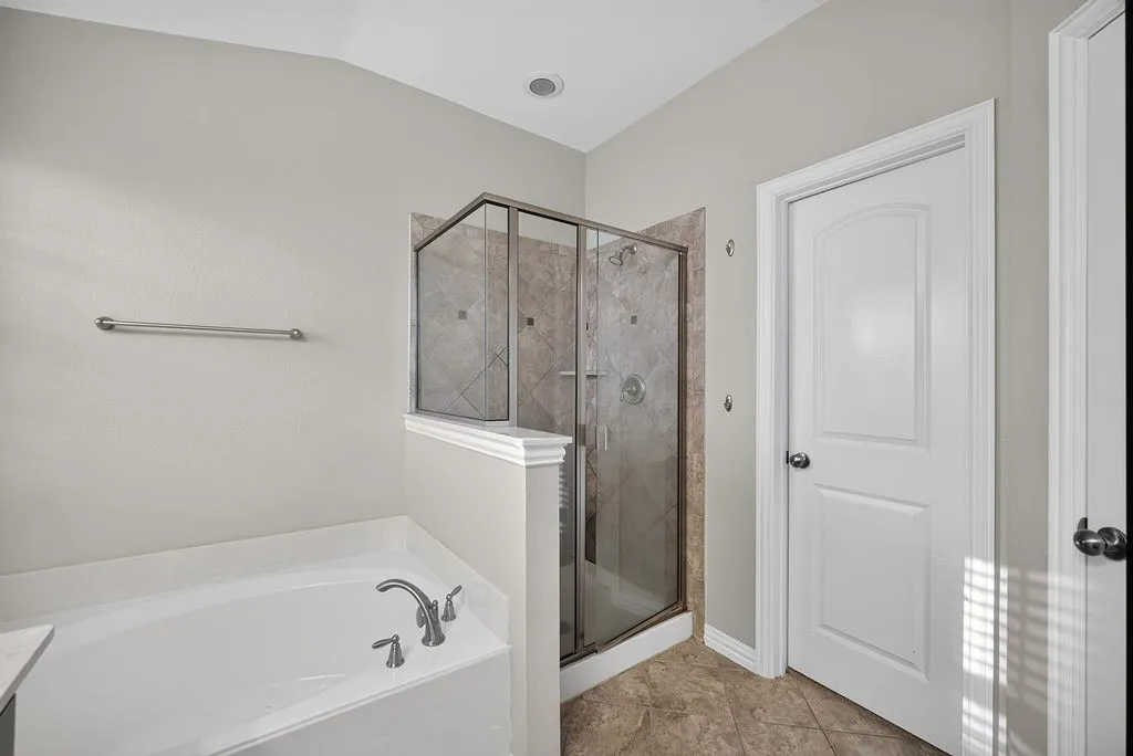 Enclosed glass-panel shower with tiled surround, adjacent soaking tub with deck-mounted faucet, and tile flooring