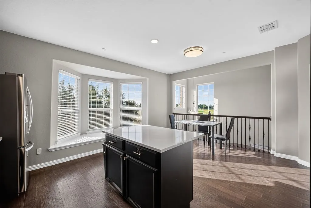 Bay window with seating, recessed lighting, wood-finish flooring, central island with solid surface countertop, and iron baluster railing