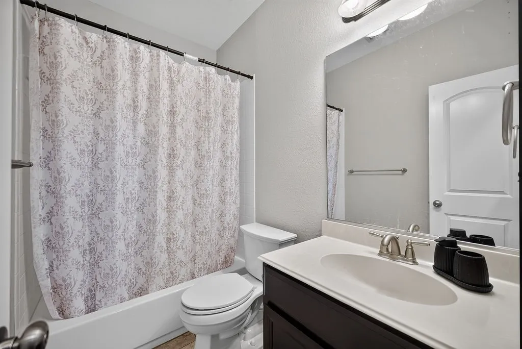 Bathtub with shower, toilet, dark wood-finish vanity with white countertop, integrated sink, and an overhead vanity light fixture