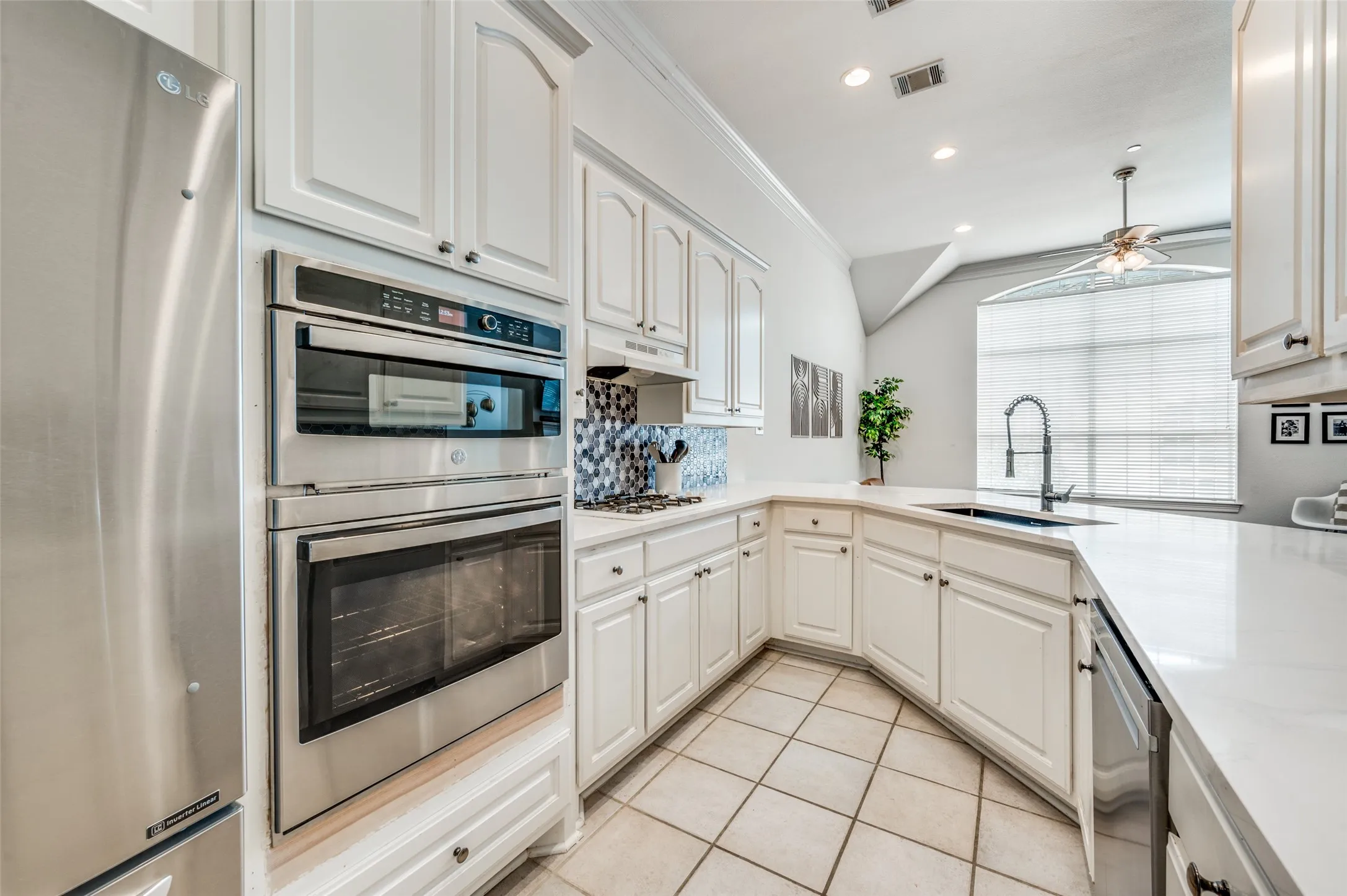 White cabinetry with brushed nickel hardware, stainless steel appliances, light-toned countertops, tile flooring, and recessed lighting