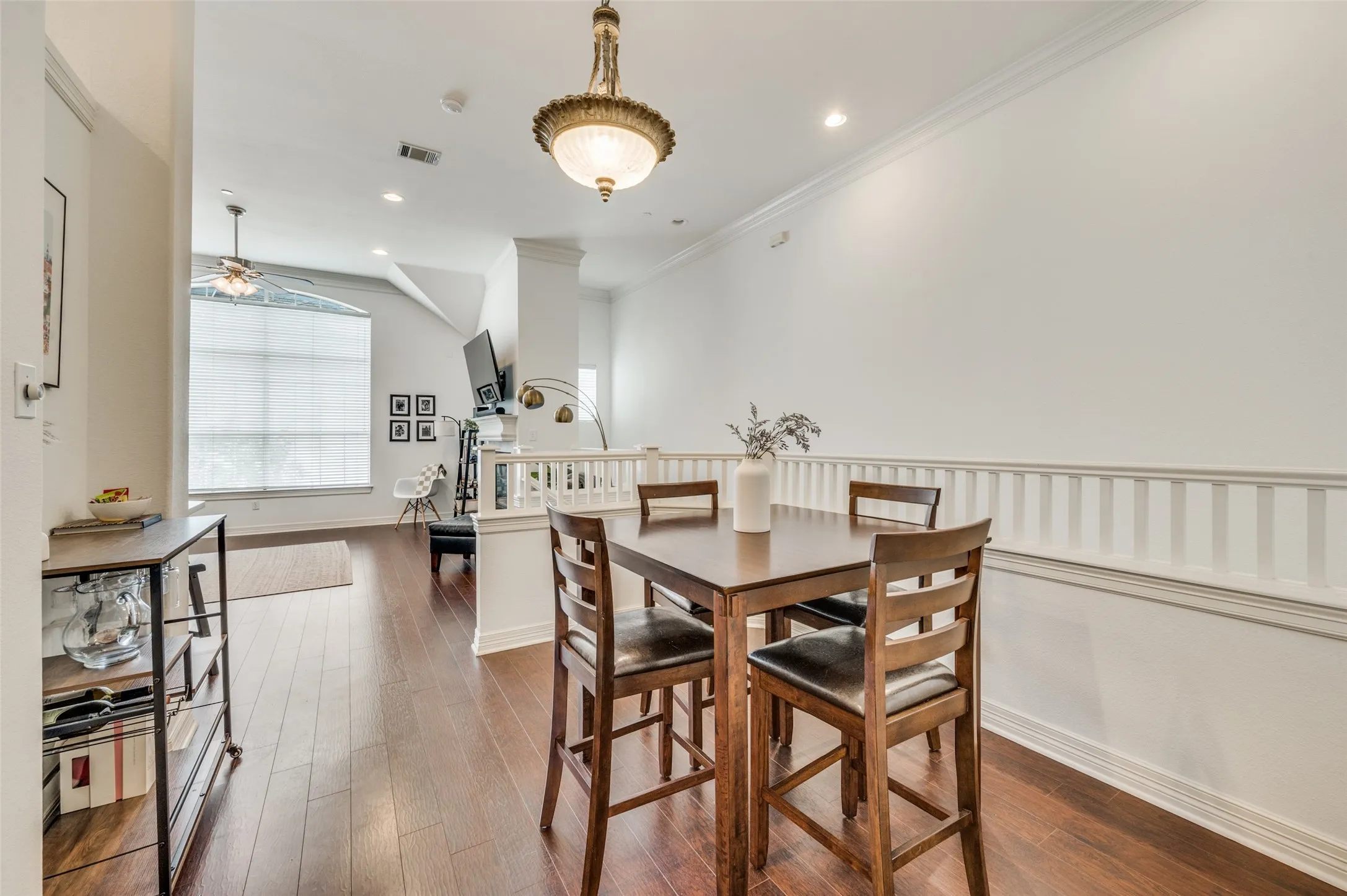 Dark wood-finish flooring throughout, recessed lighting, crown molding, and a decorative railing