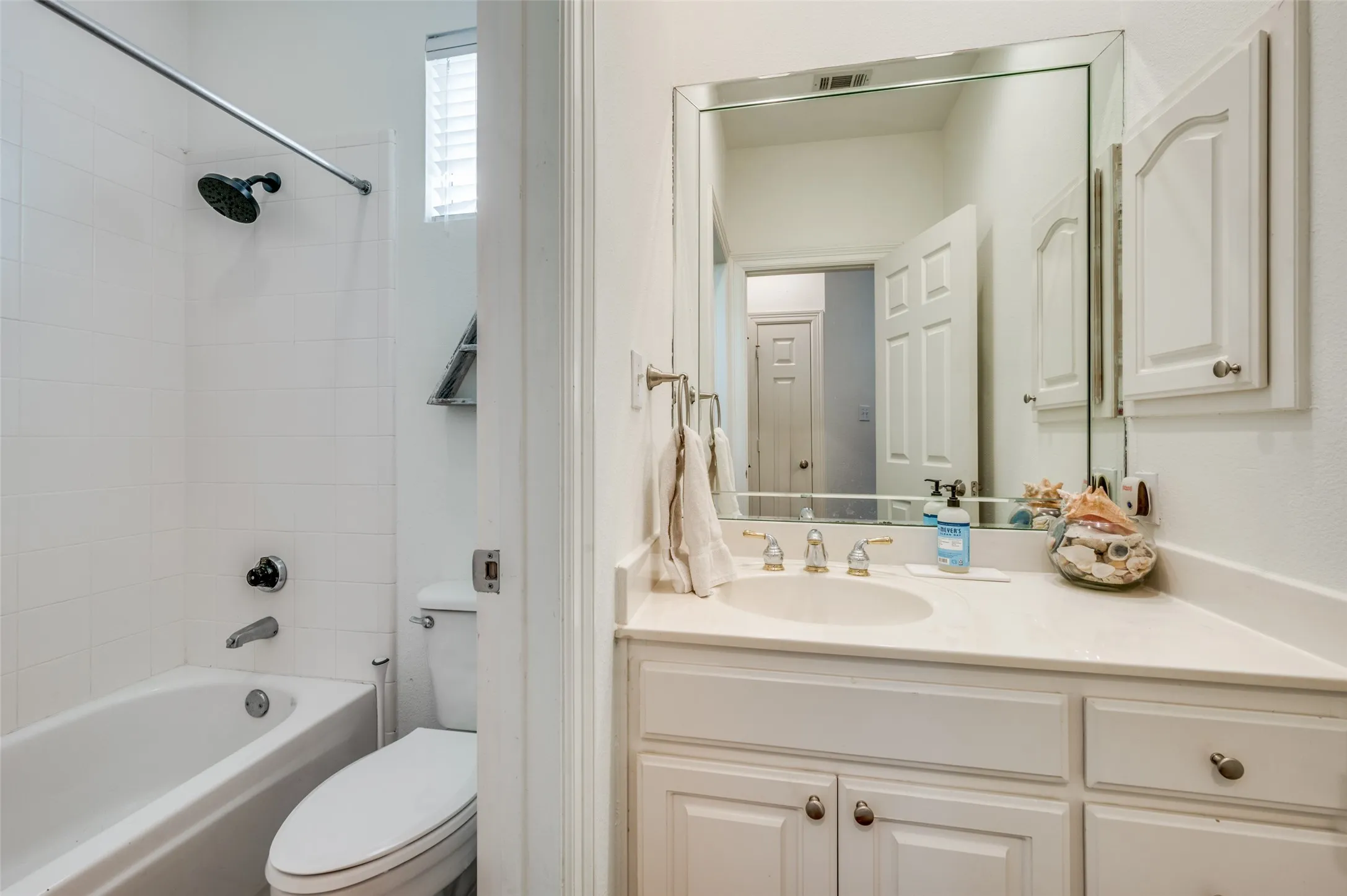Bathroom featuring a built-in tub with tile surround, a single vanity with an undermount sink, and a framed mirror