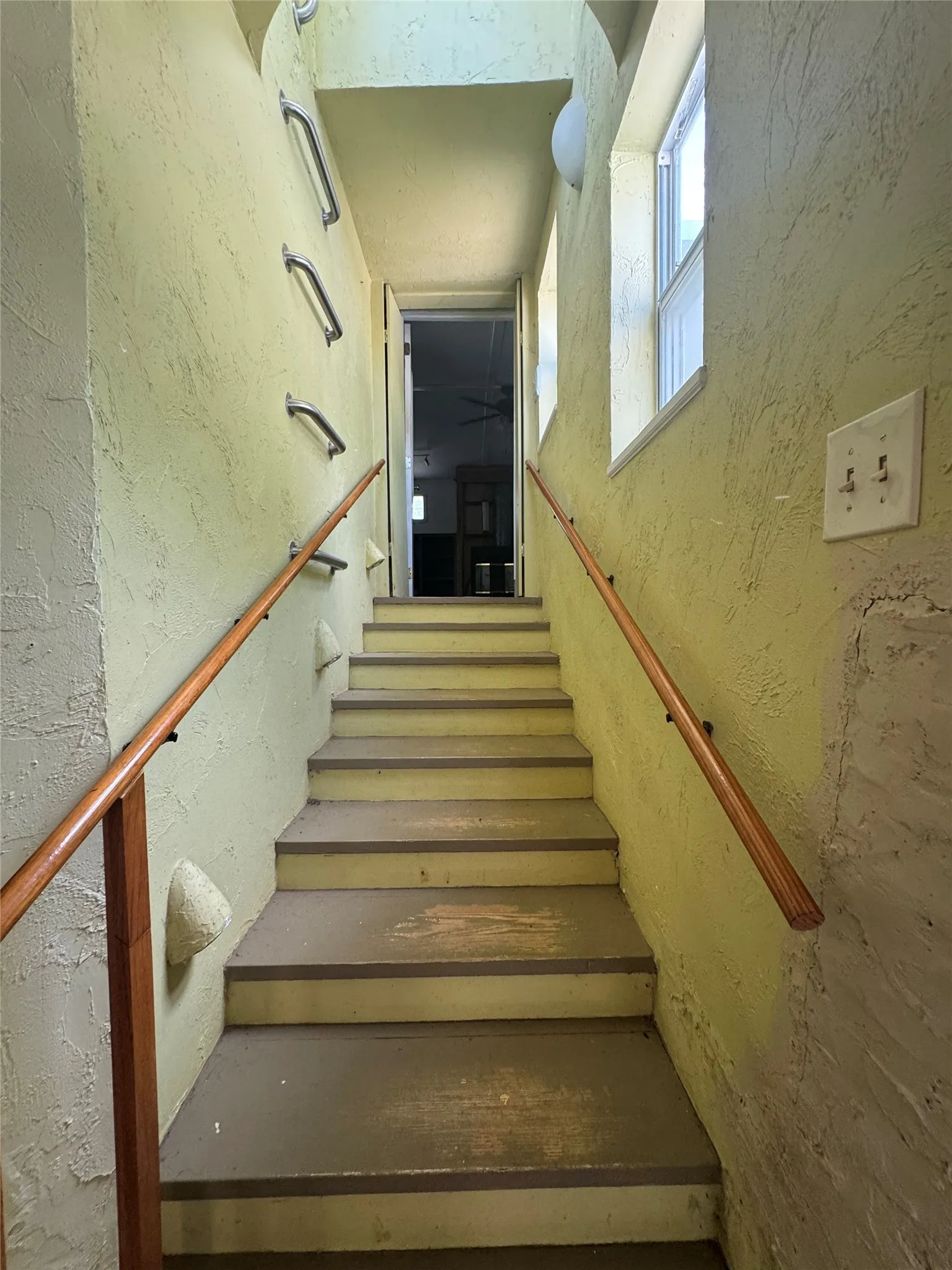 Staircase featuring wood handrails, textured wall finish, and overhead lighting
