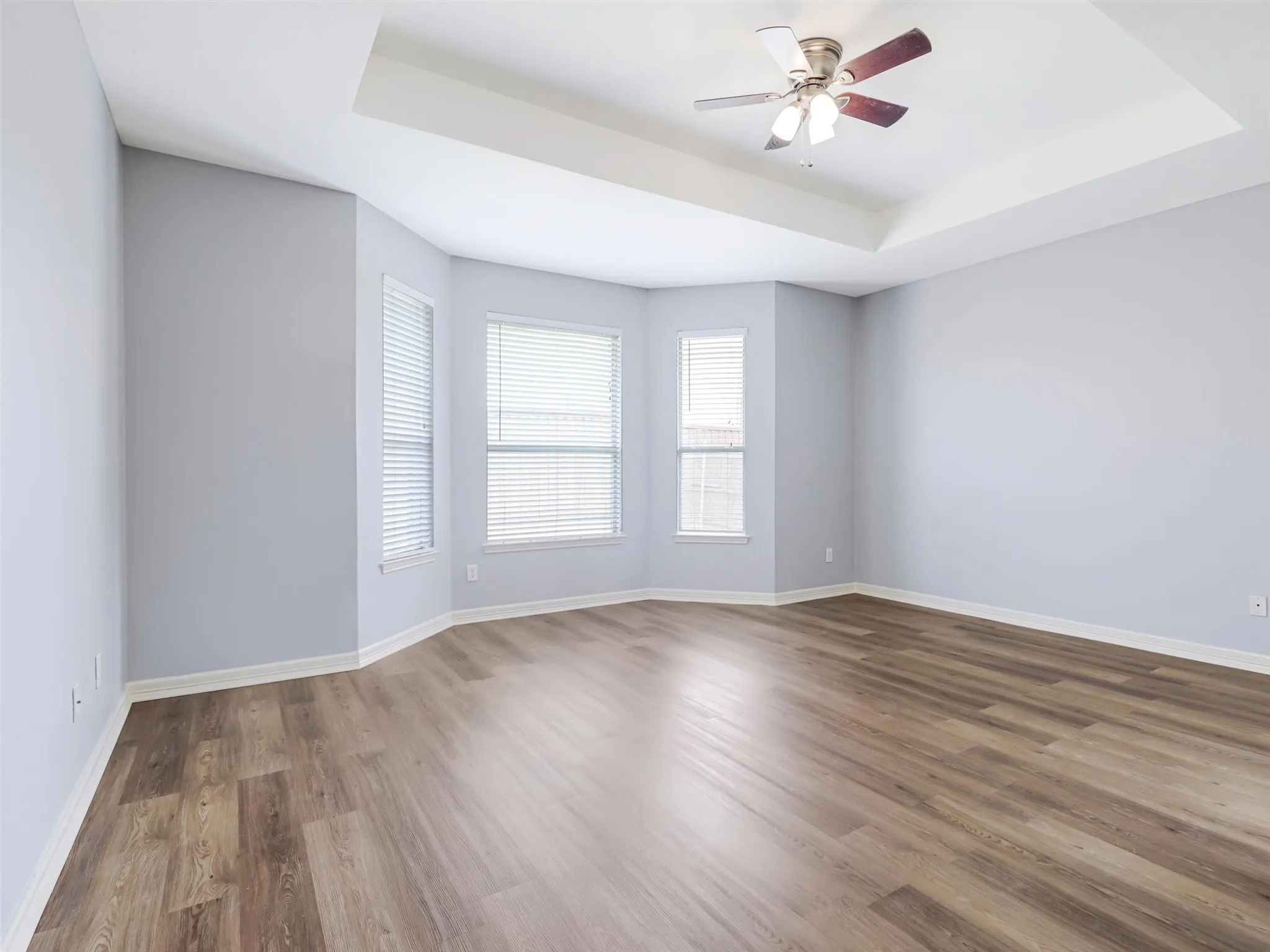 Tray ceiling with a ceiling fan, wood-finish flooring, and multiple windows with blinds