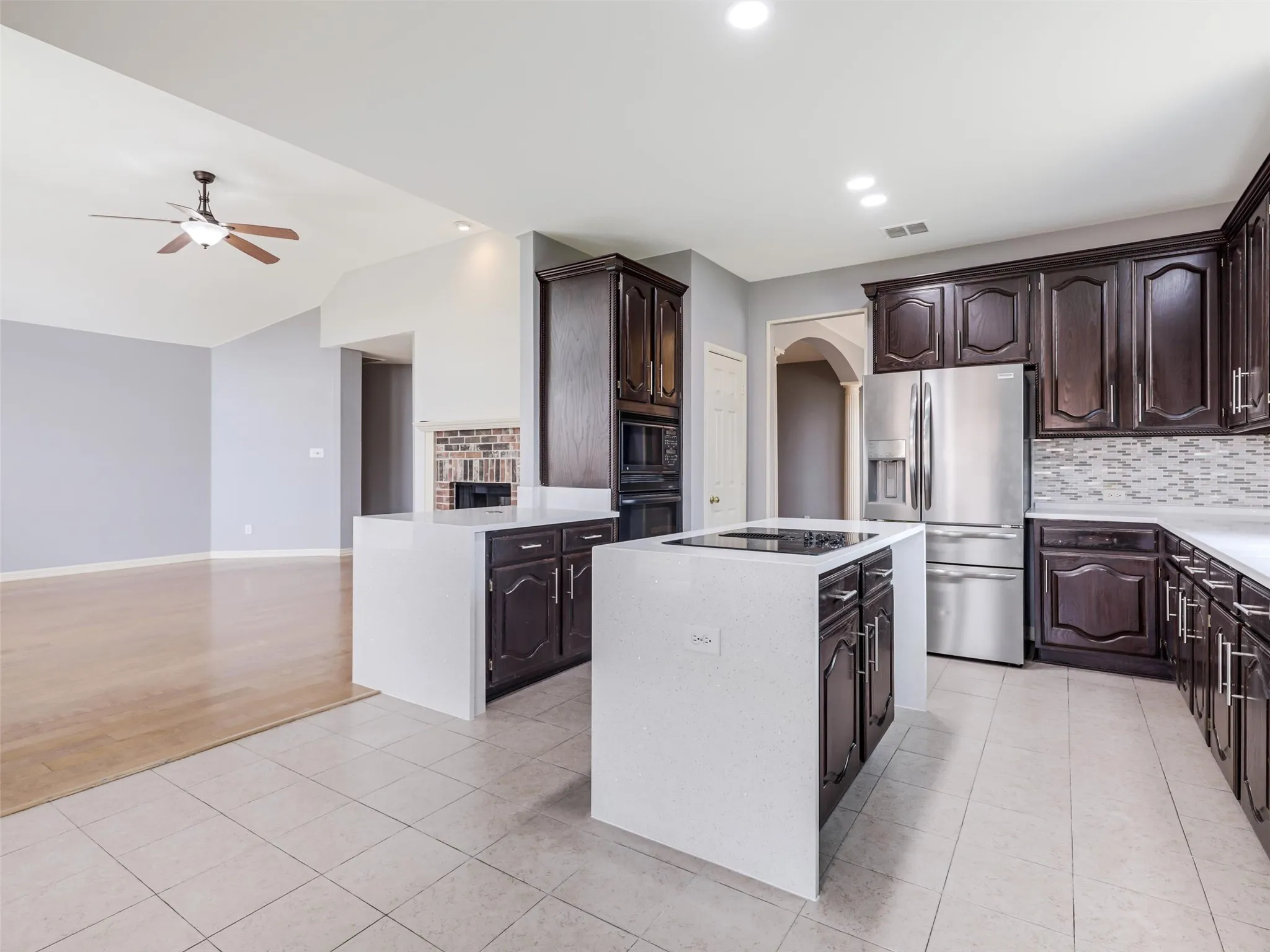 Kitchen featuring dark wood cabinetry, stainless steel appliances, a center island with a cooktop, white countertops, and a tiled backsplash