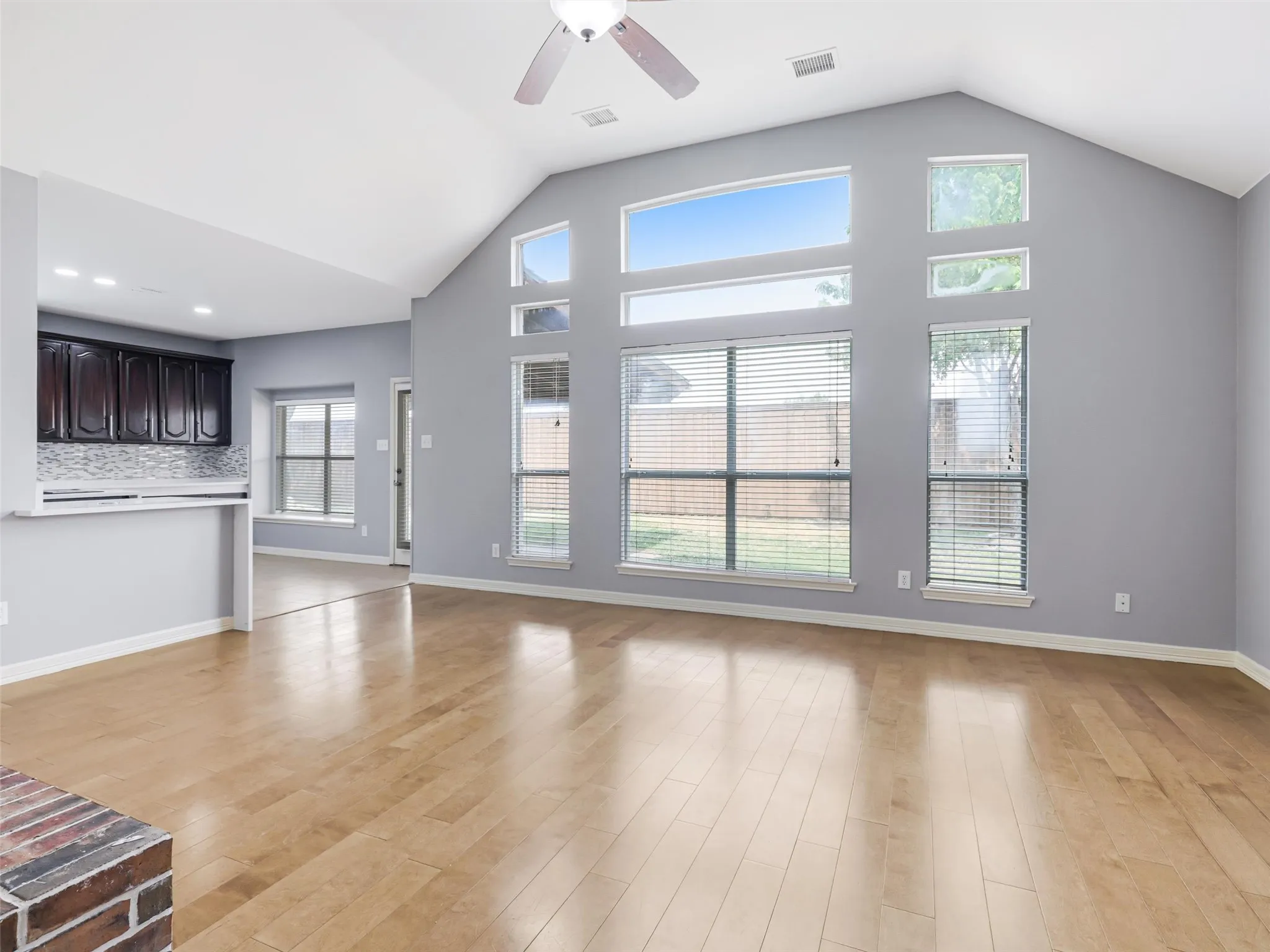 Vaulted ceiling with a ceiling fan, light wood-finish flooring, and a window wall