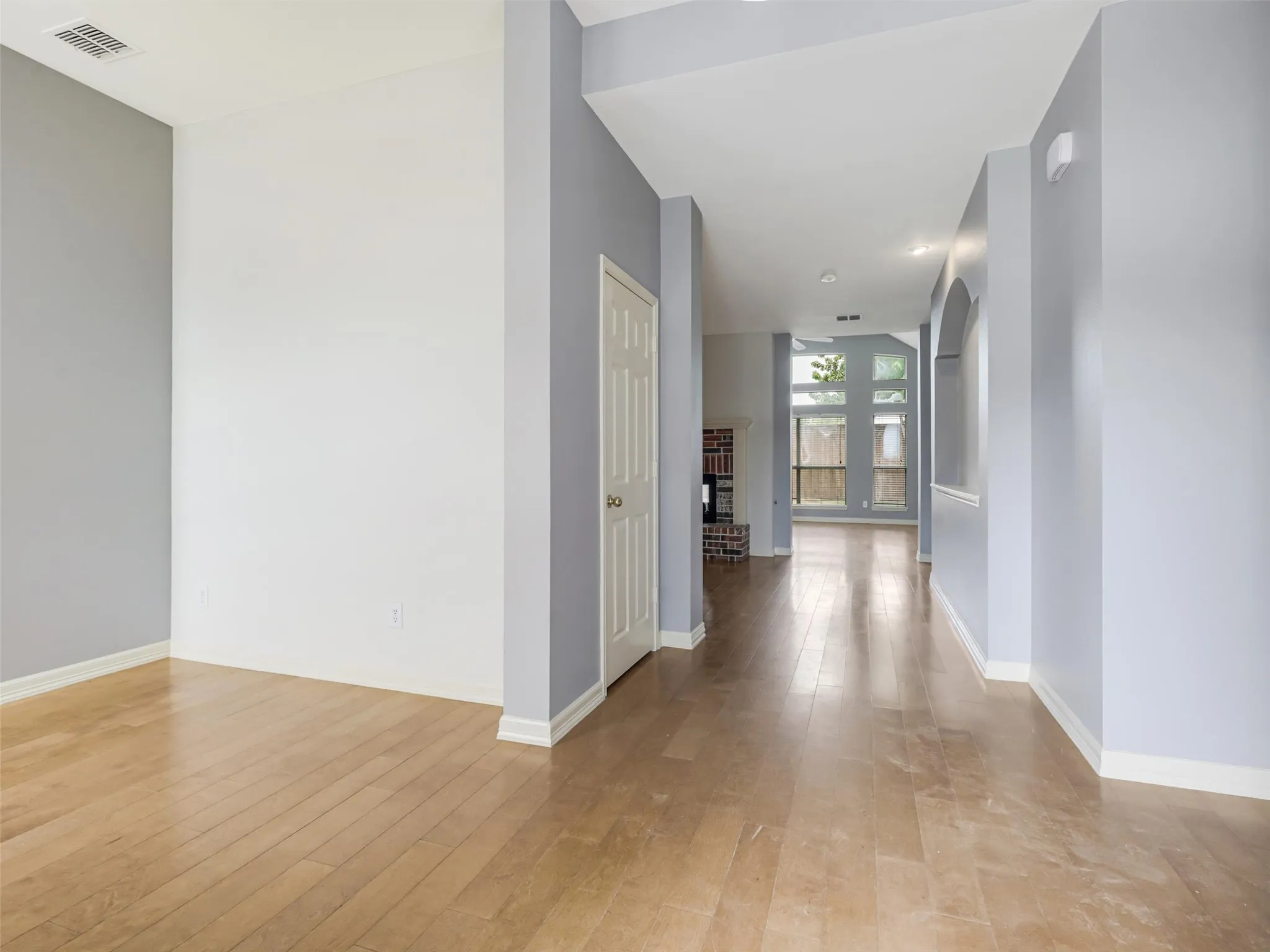 Wood-finish flooring throughout, light gray and white wall palette, and an arched hallway entry