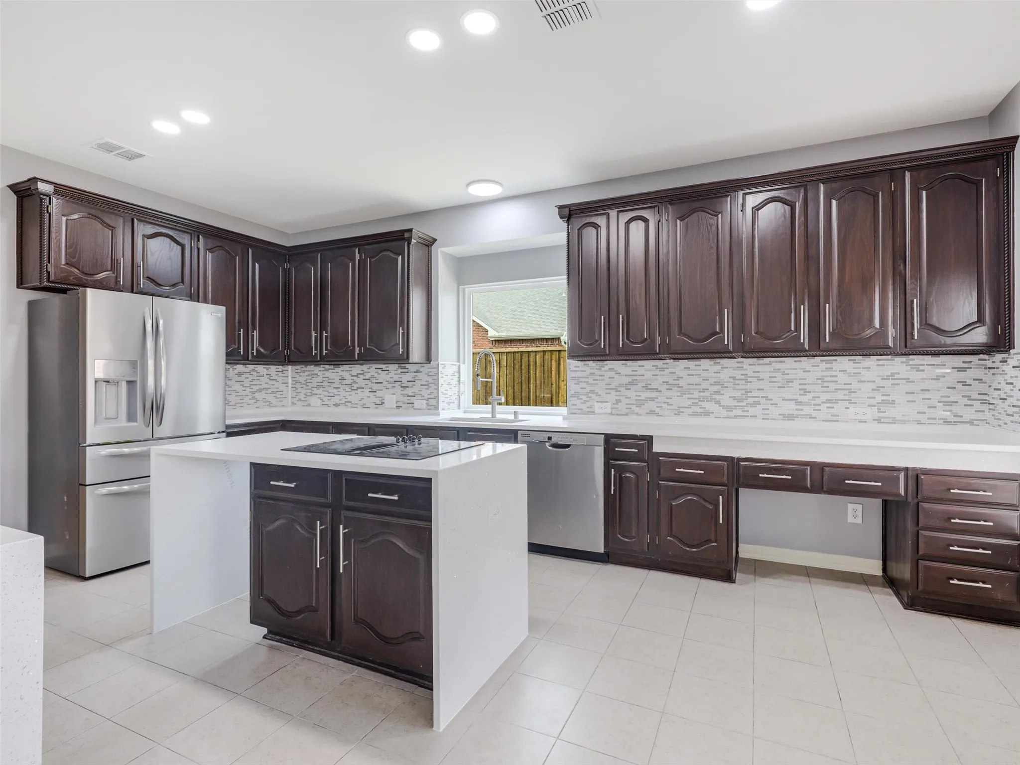 Dark wood-finish cabinetry, stainless steel appliances, white countertops, tile flooring, and a mosaic tile backsplash
