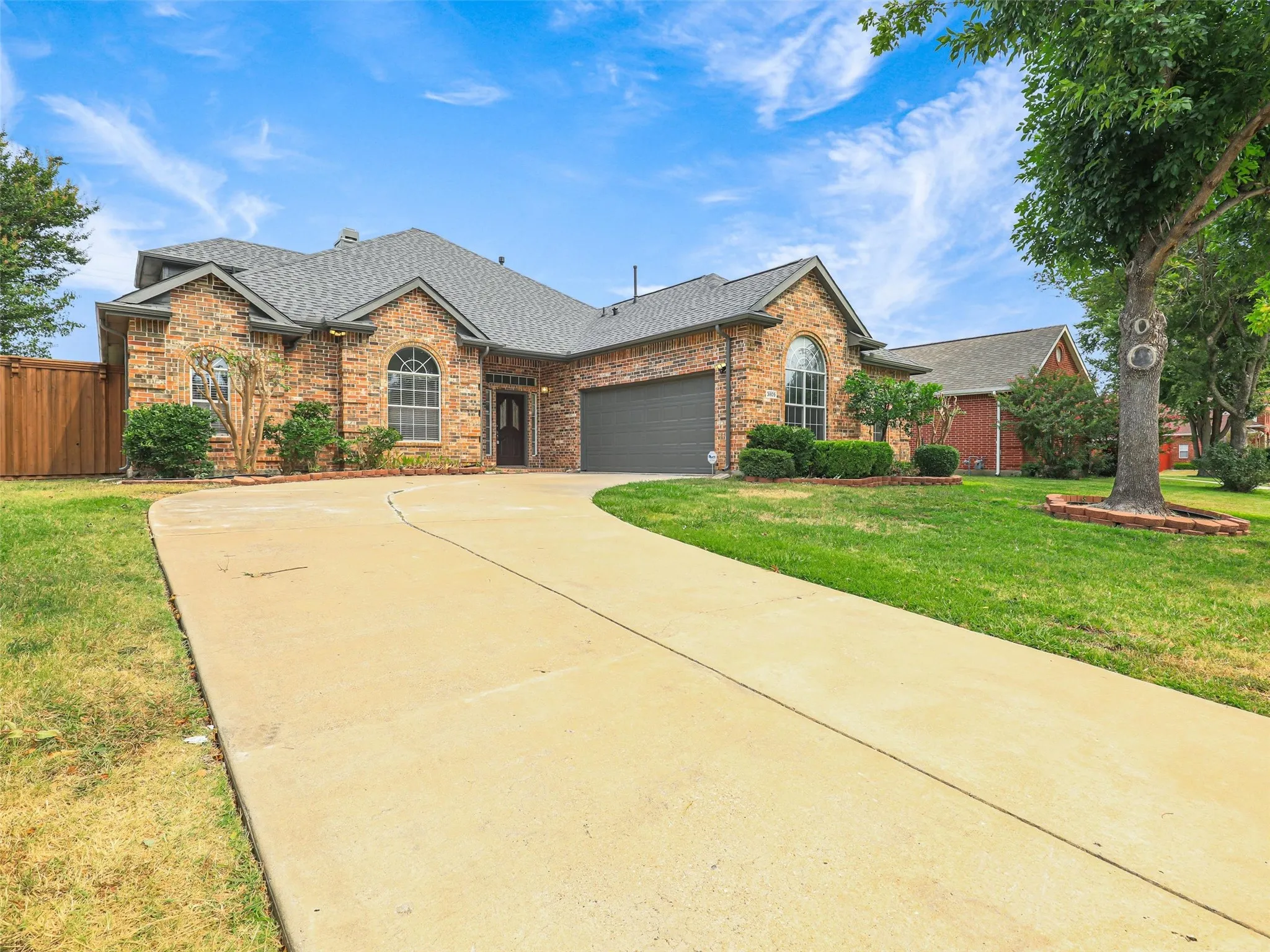 Brick exterior with arched windows, mature landscaping, and an attached garage