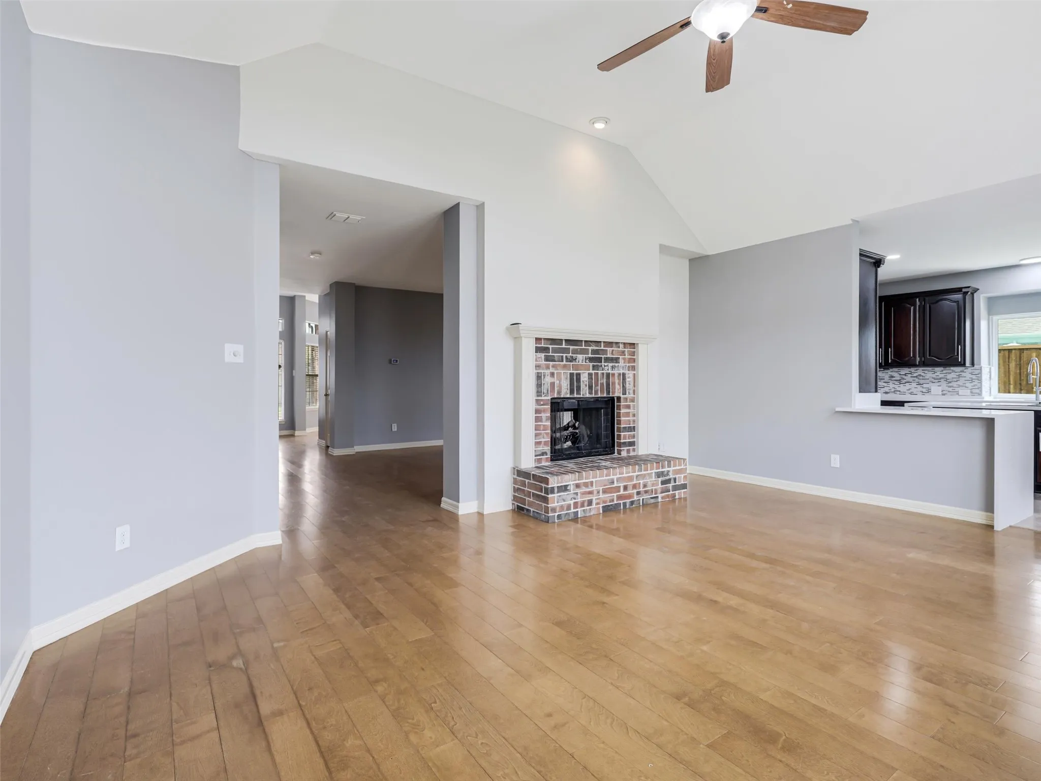 Vaulted ceiling featuring a ceiling fan, brick fireplace with hearth, and wood-finish flooring
