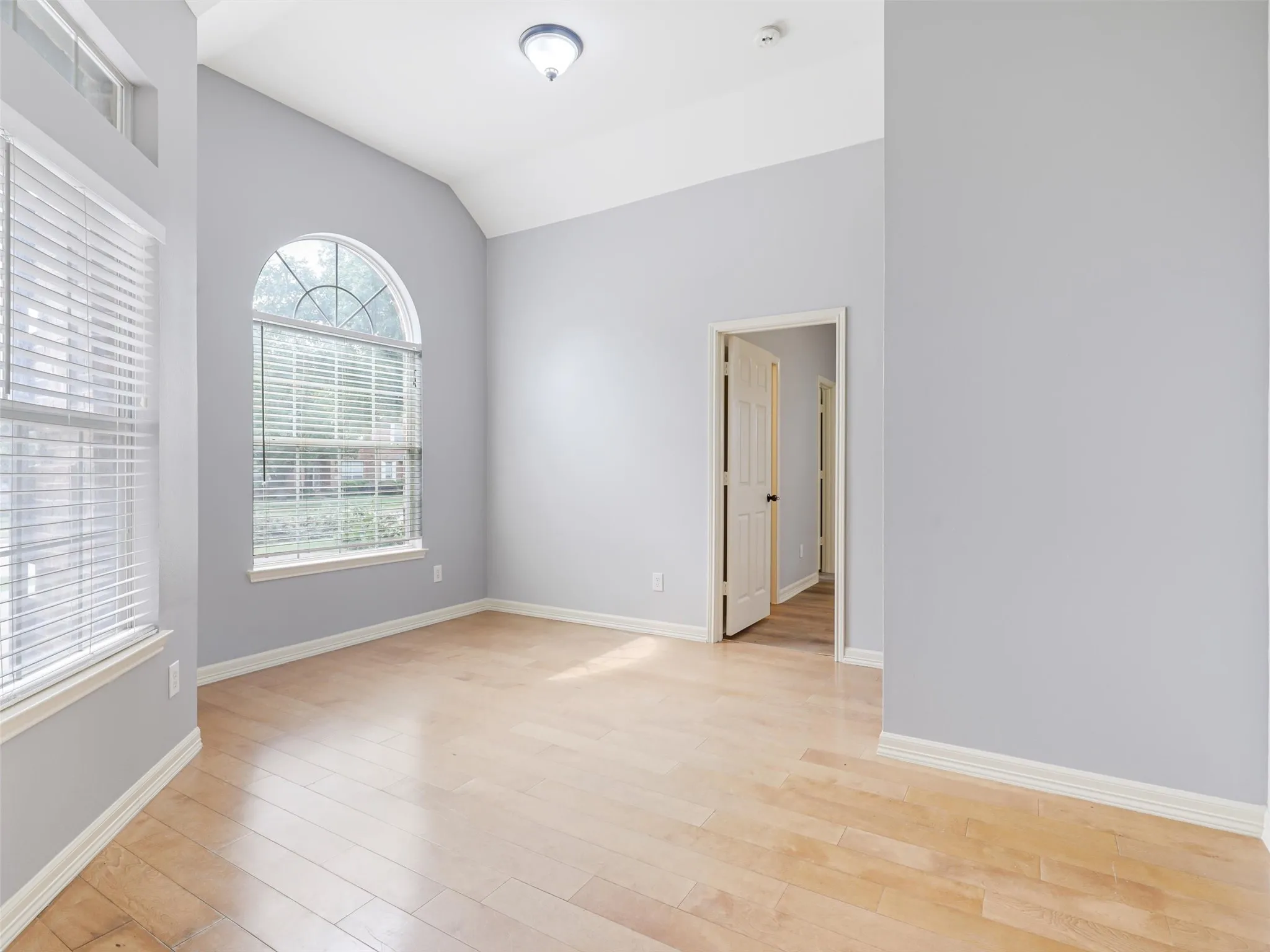 Vaulted ceiling with an arched window and transom window, light wood-finish flooring, and a flush-mount ceiling light fixture