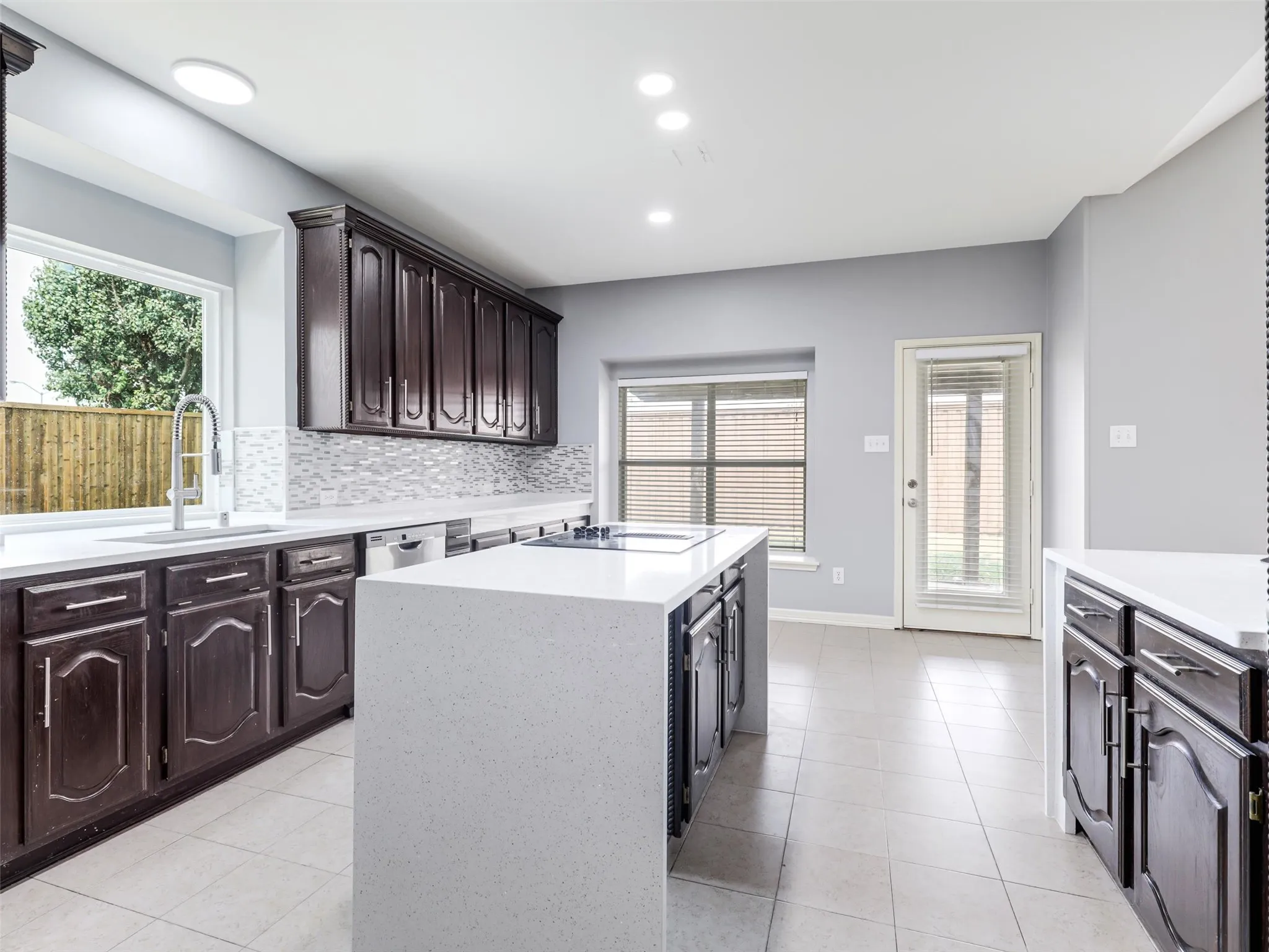 Kitchen featuring a center island, dark wood-finish cabinetry, light-toned countertops, and a full tile backsplash