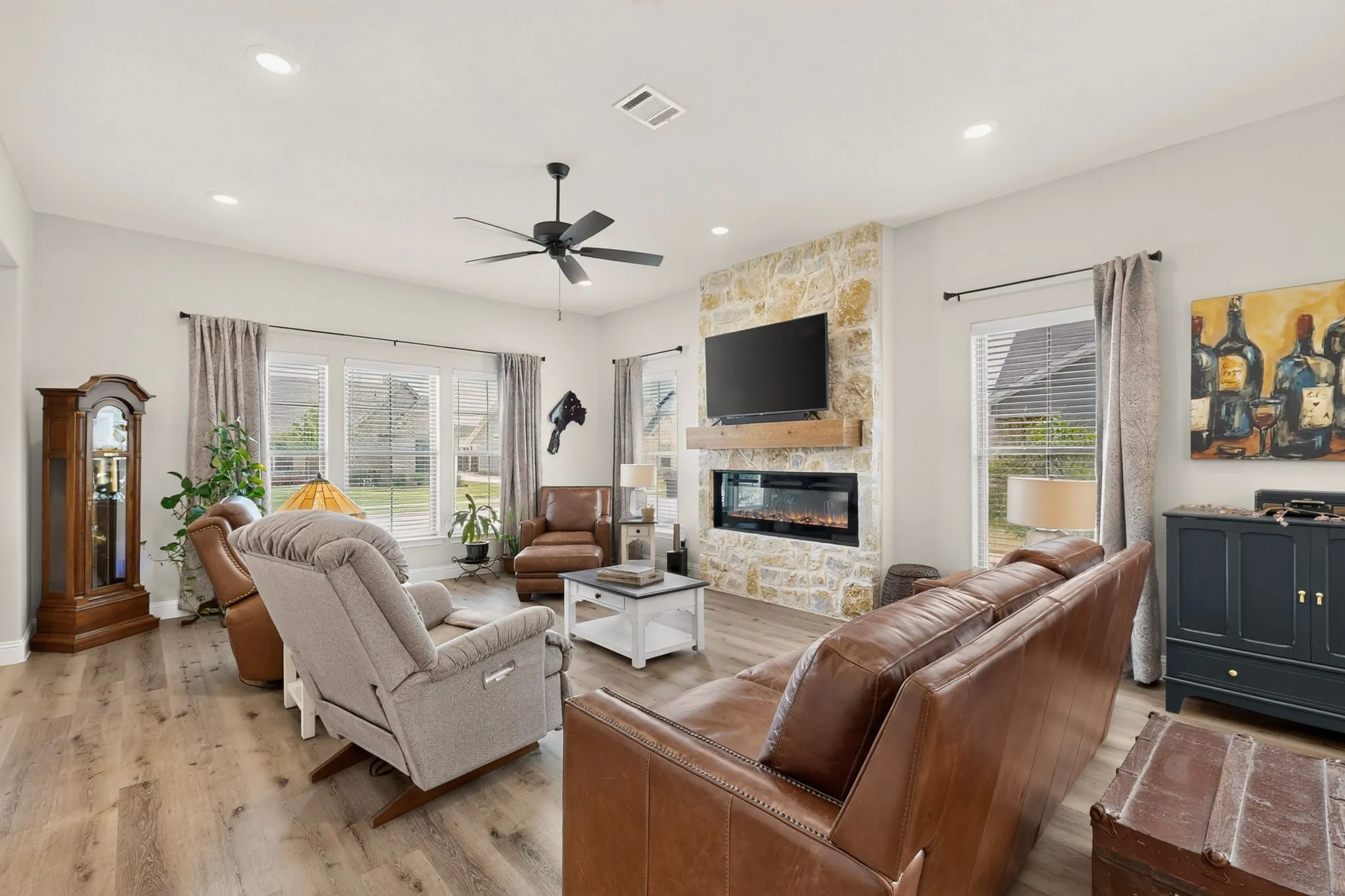 Spacious living area featuring wood-finish flooring, a stone accent wall, a built-in electric fireplace, and recessed lighting