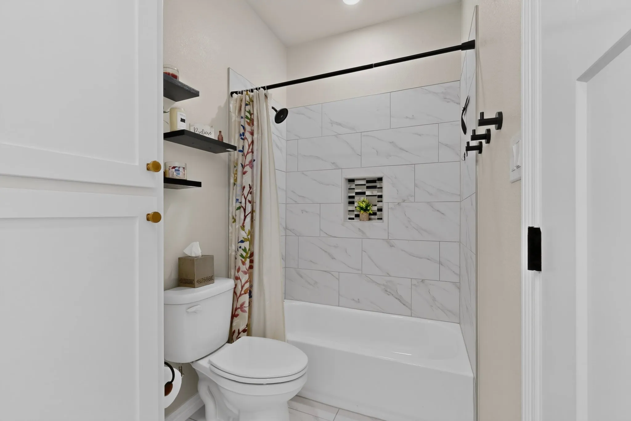 Bathroom featuring a built-in tub with a tile surround, black shower fixtures, recessed shower niche with mosaic tile, and floating shelves