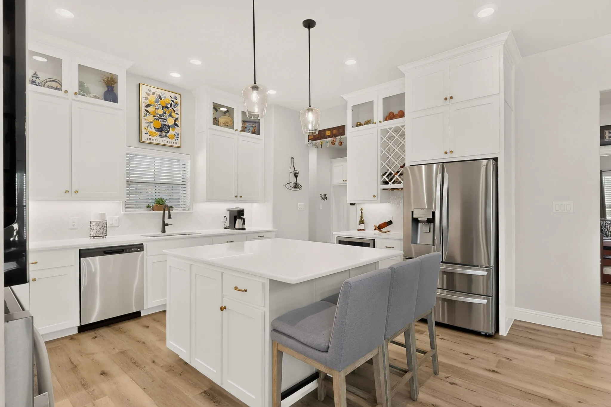 White shaker cabinetry floor to ceiling with glass uppers, quartz  counters, stainless steel appliances, Induction cooktop, convection oven, central island with seating, pendant lighting, and wood-finish flooring