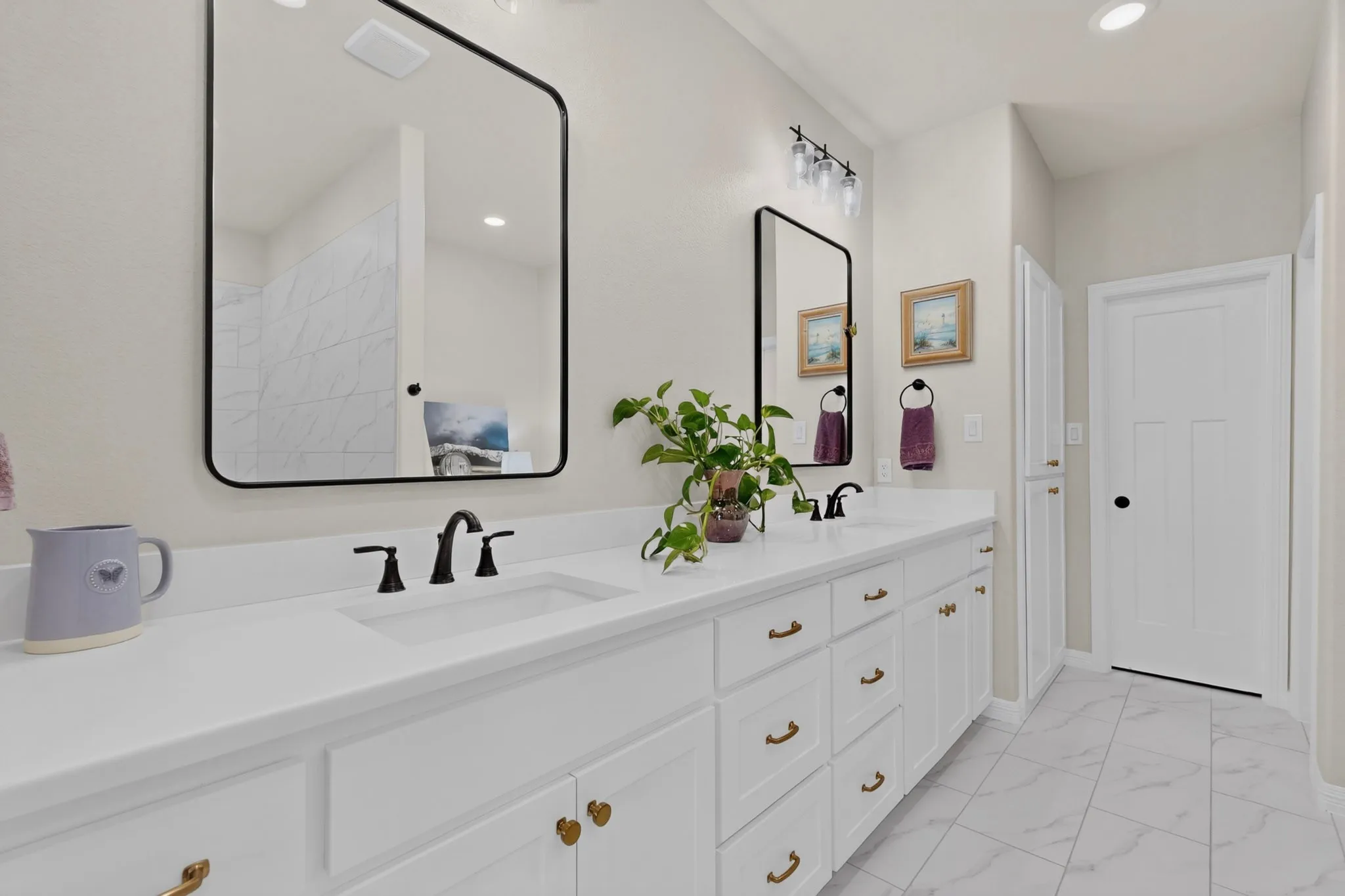 Dual vanity with integrated sinks, oil rubbed bronze, framed mirrors, and large built in linen cabinetry, walk in closet