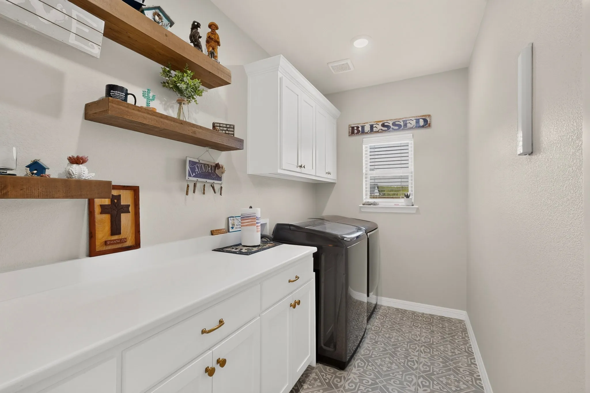 White cabinetry with brass hardware, wood-finish floating shelves, white countertop, and patterned floor tile