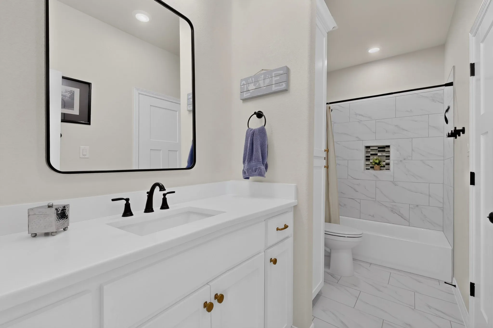 Vanity with a rectangular undermount sink, beautiful tile on floor and tub surround with niche