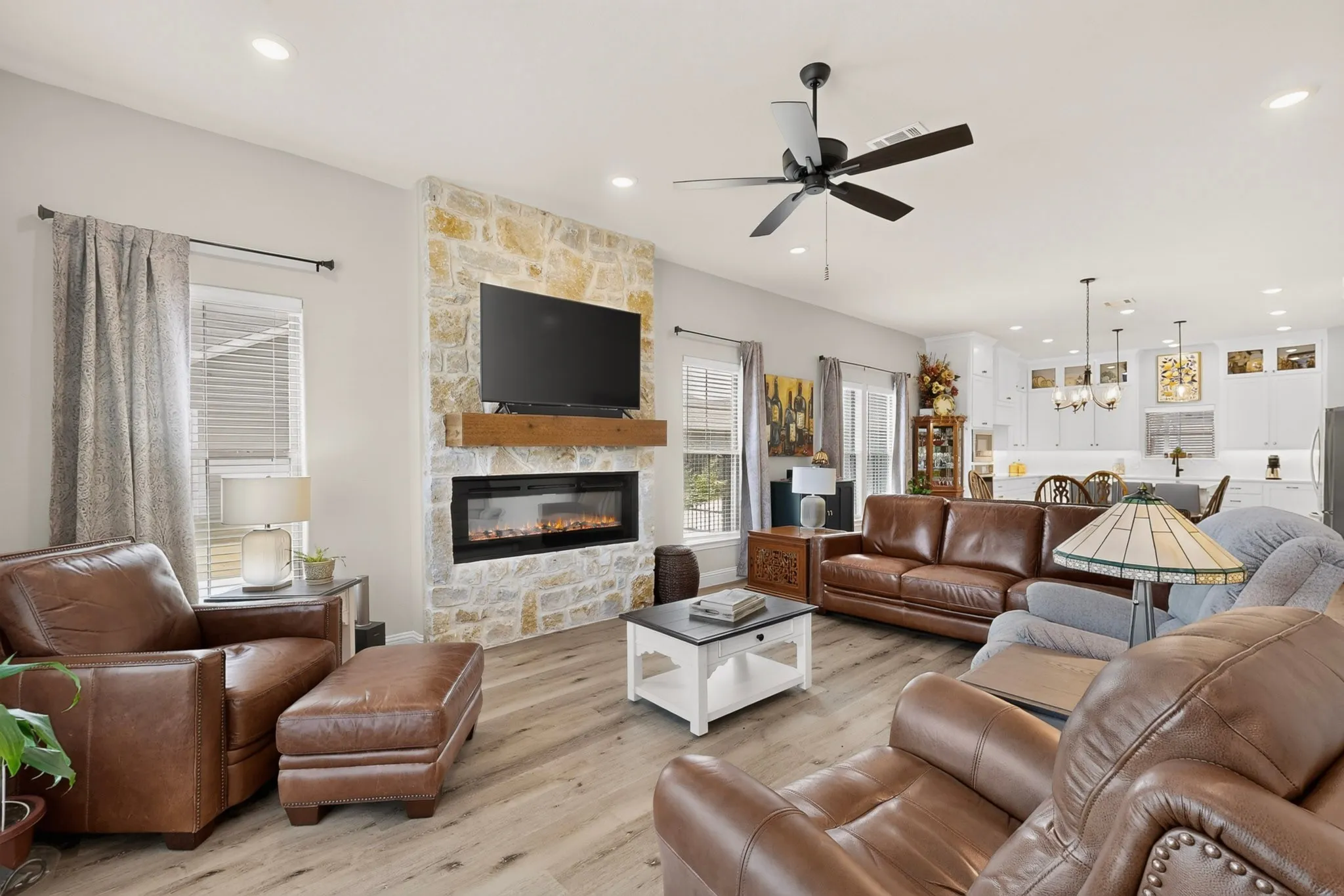 Open-concept living area featuring a stone accent wall with a built-in electric fireplace, recessed lighting, and wood-finish flooring