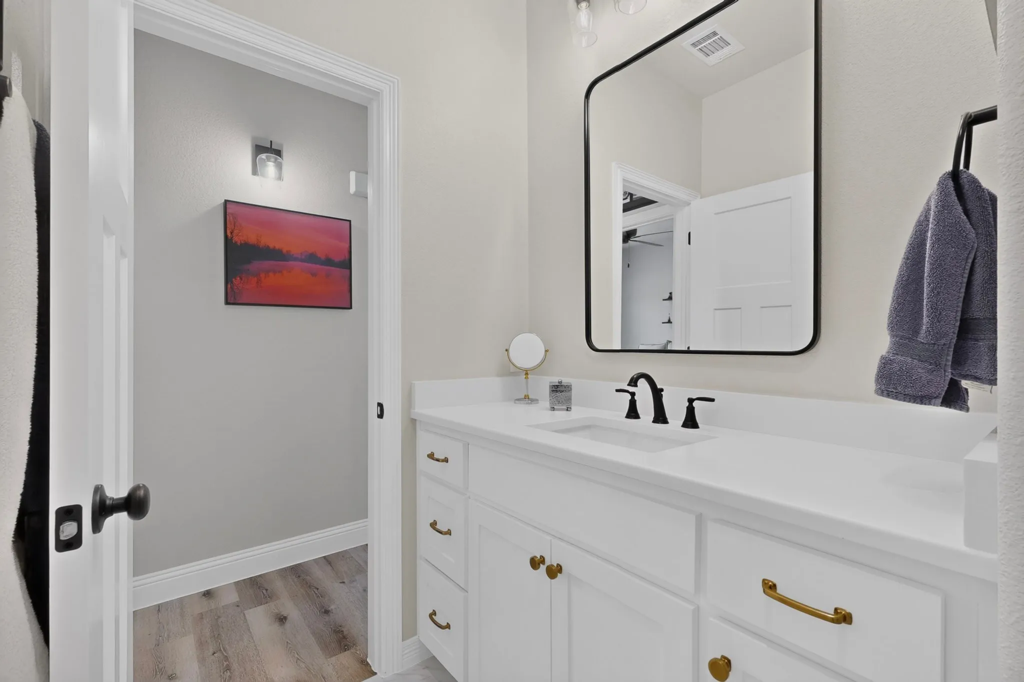 White vanity with integrated sink, black framed mirror, black wall-mounted faucet, and gold-tone hardware