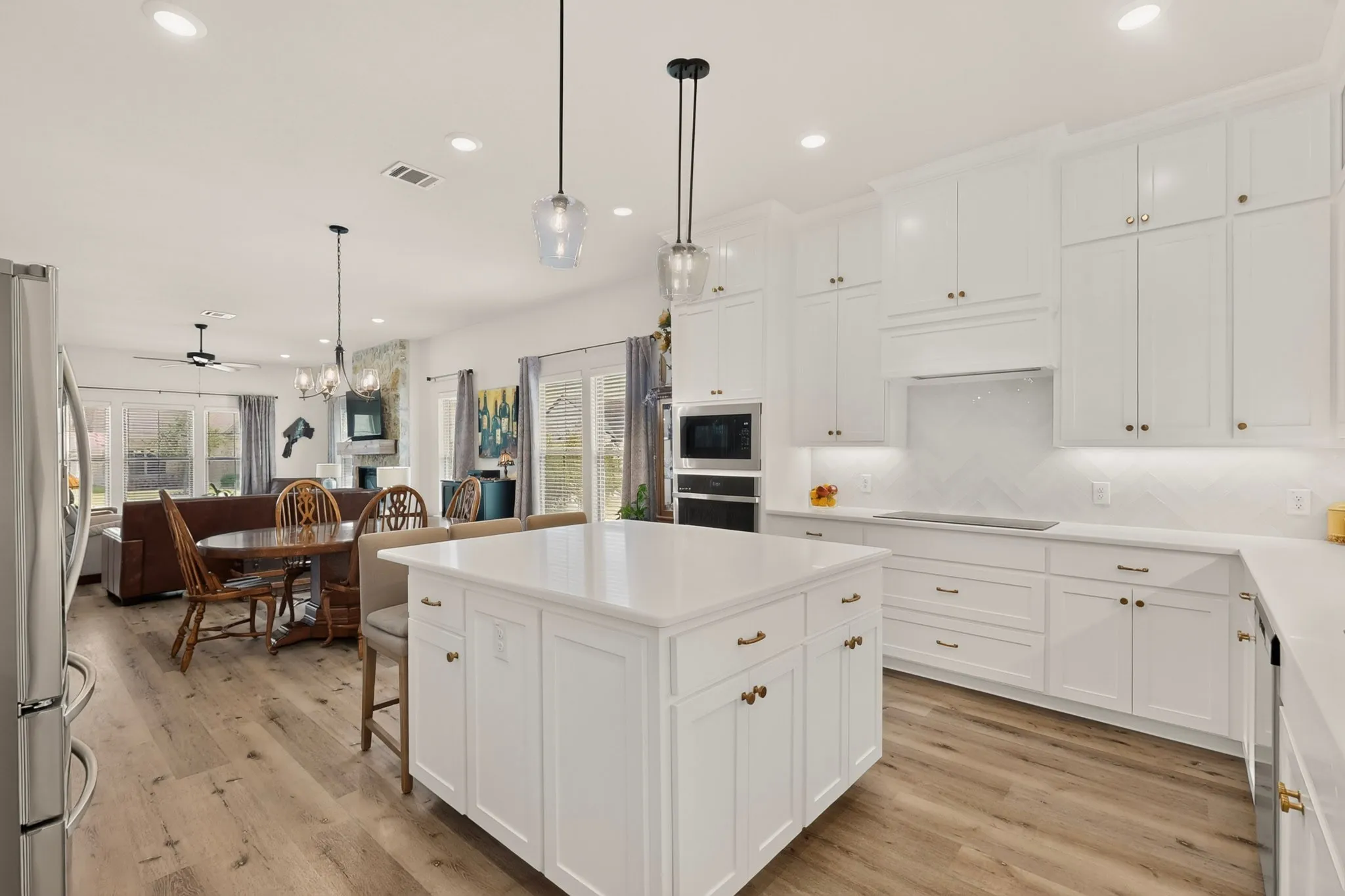 Open-concept layout featuring a kitchen island, recessed lighting, wood-finish flooring, white cabinetry, and stainless steel appliances