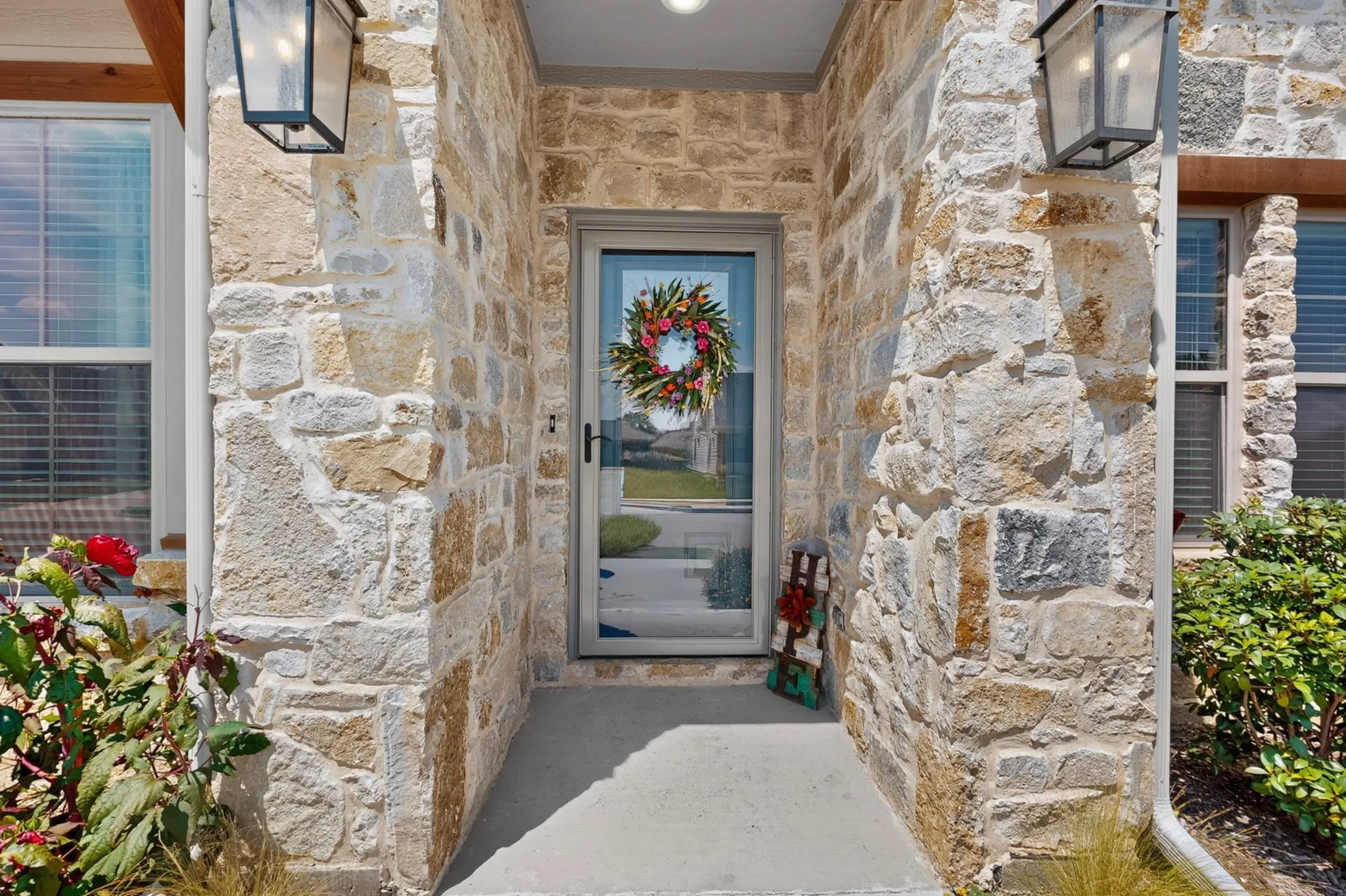 Stone facade featuring integrated porch lighting, Storm door, and decorative window blinds