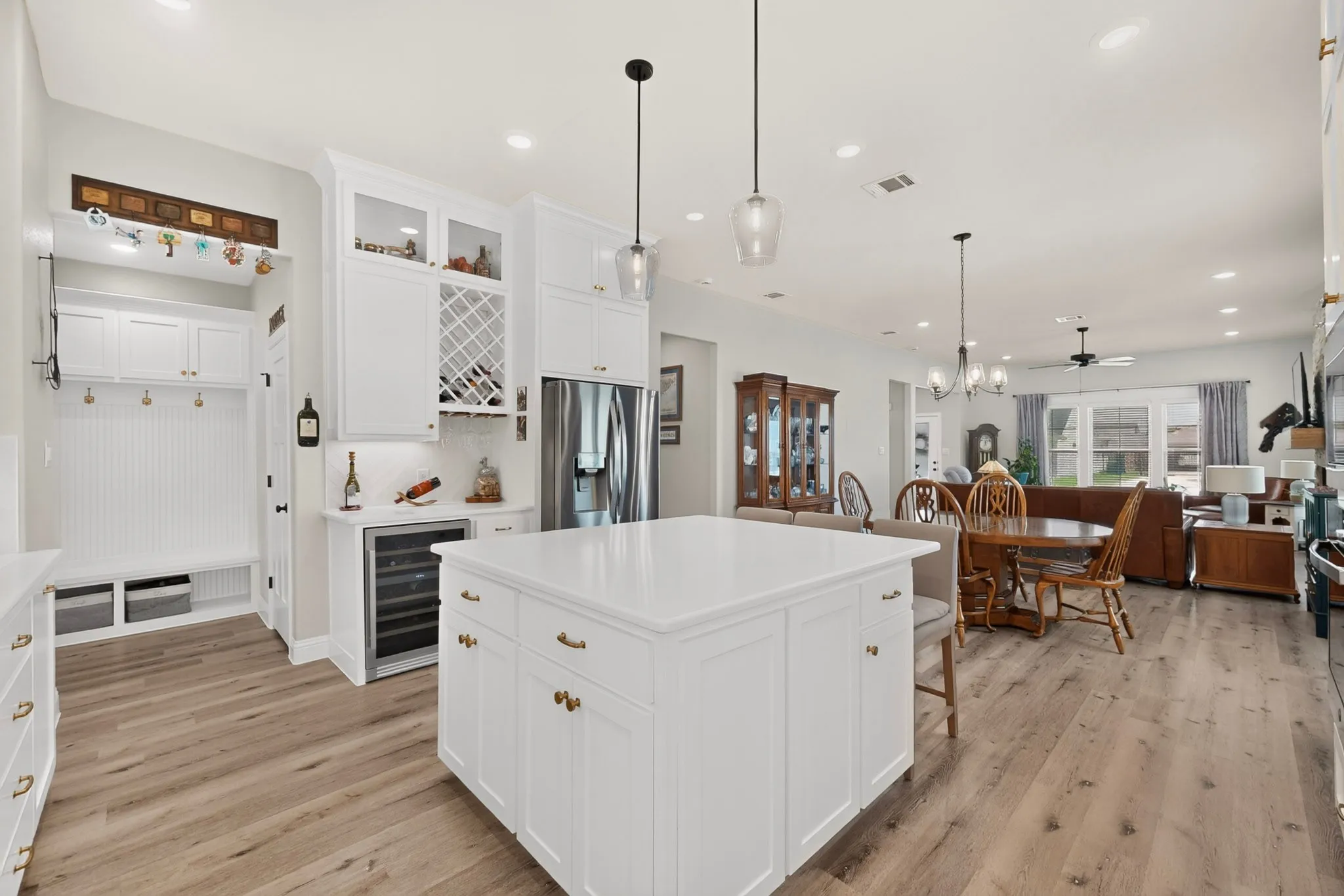 Spacious kitchen island with white cabinetry, wood-finish flooring, recessed lighting, and a built-in wine refrigerator, mud bench and walk in pantry