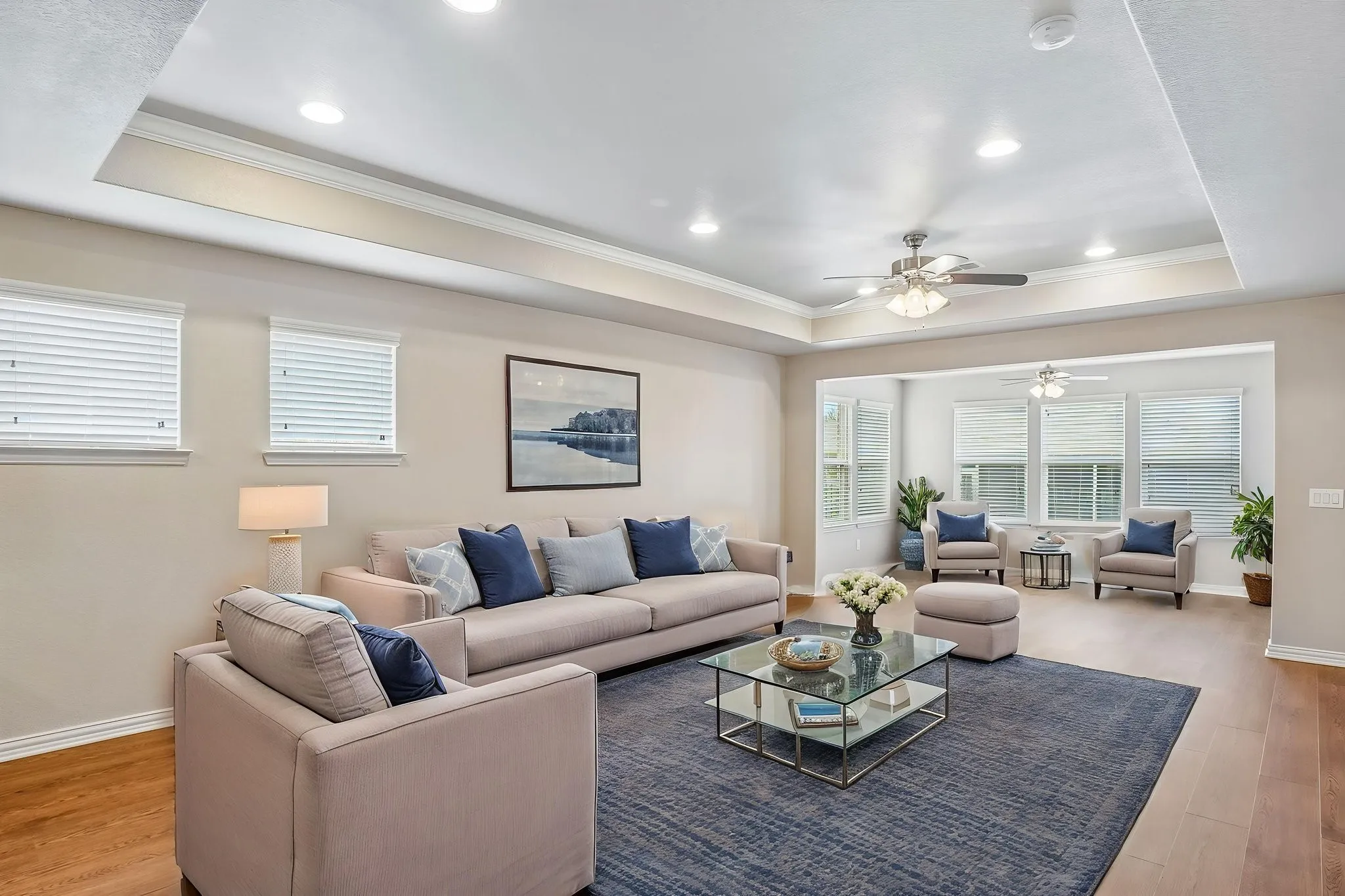 Recessed lighting, tray ceiling, ceiling fans, wood-finish flooring, and multiple windows with blinds