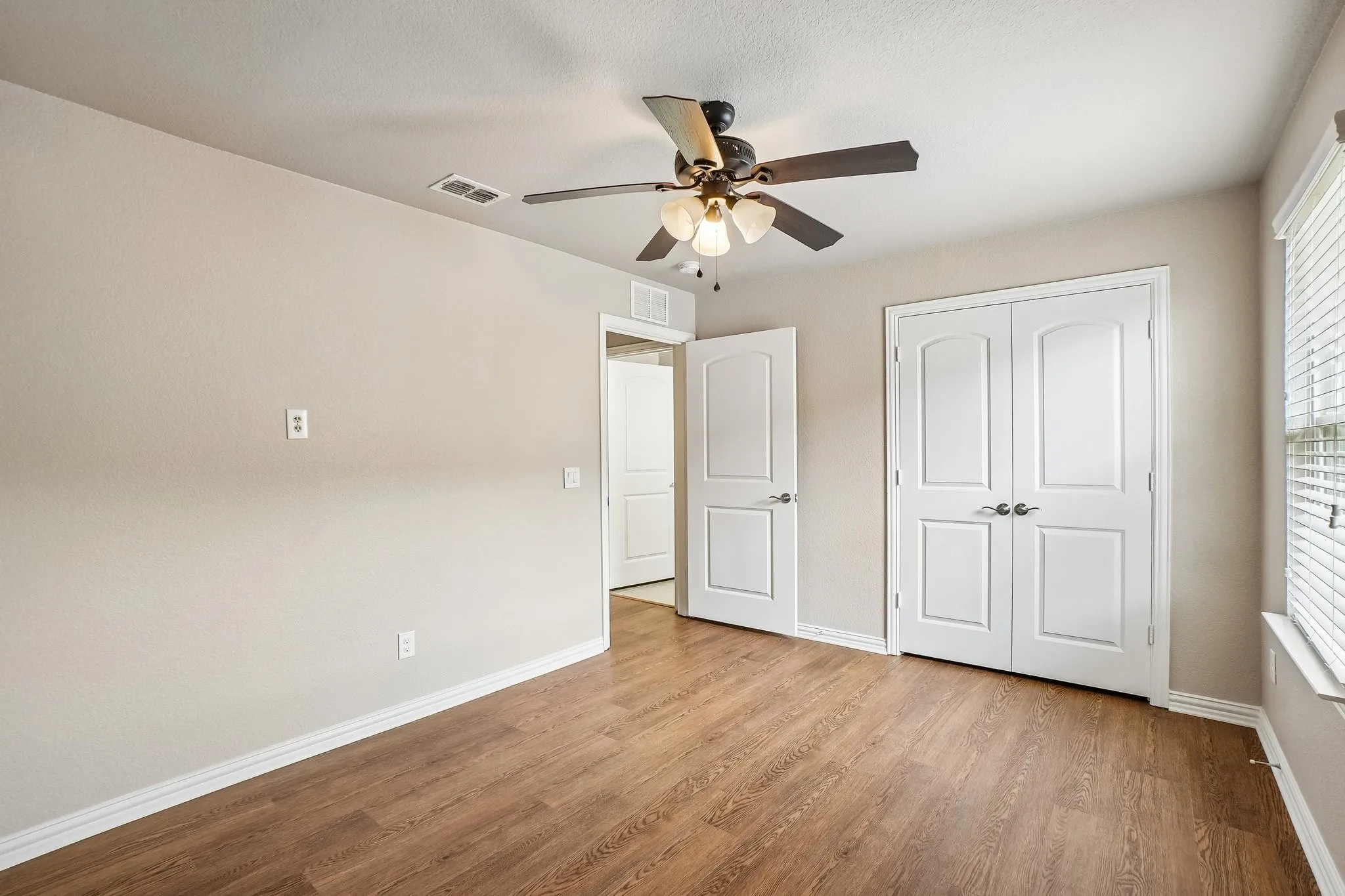Wood-finish flooring, ceiling fan with integrated lighting, white paneled doors, and window with horizontal blinds