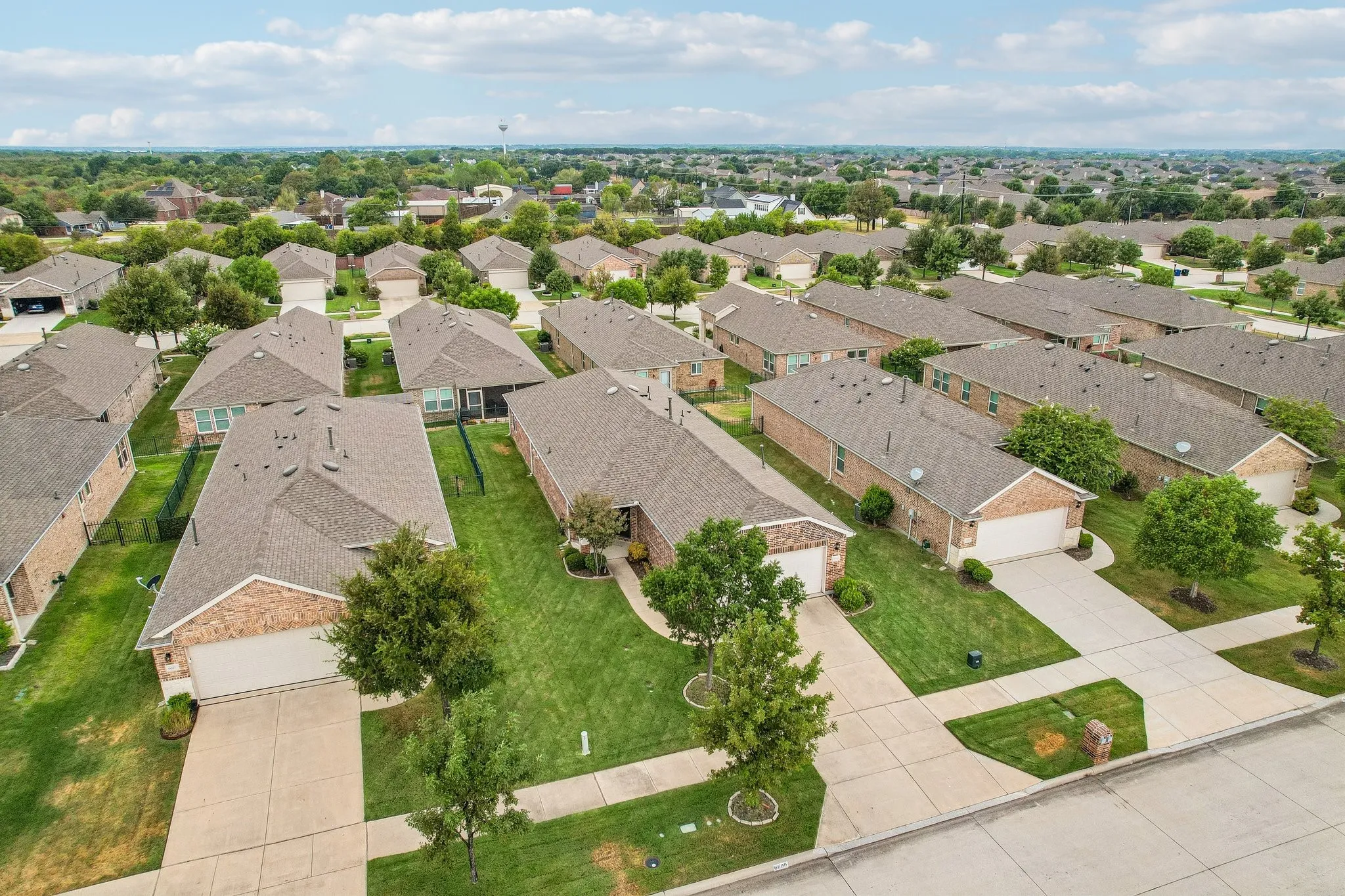 Aerial perspective of a residential community with established homes, each featuring brick and siding exteriors, attached garages, and paved driveways