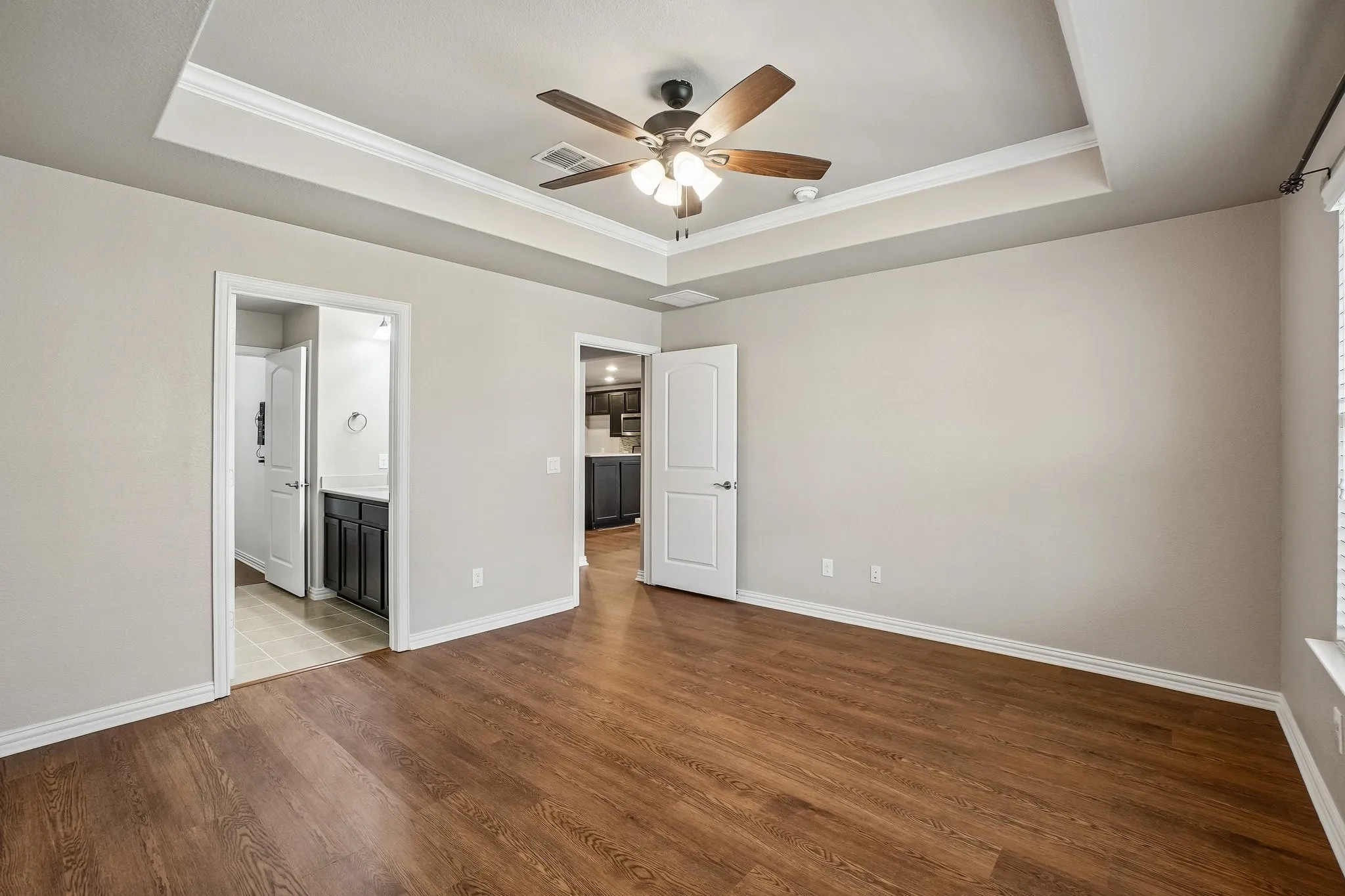 Tray ceiling with crown molding, wood-finish flooring, ceiling fan, and window with blinds