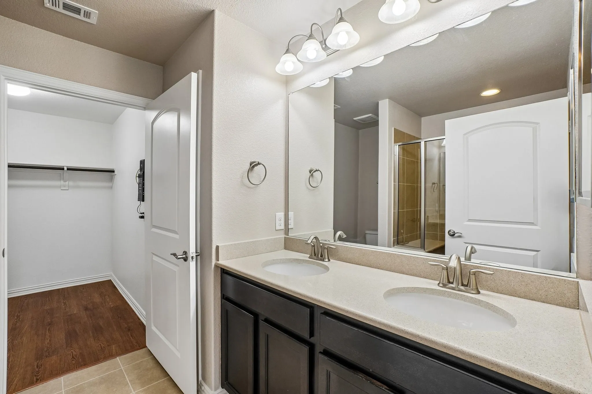 Dual vanity with integrated sinks and brushed nickel faucets, expansive mirror, sconce lighting, and wood-finish flooring