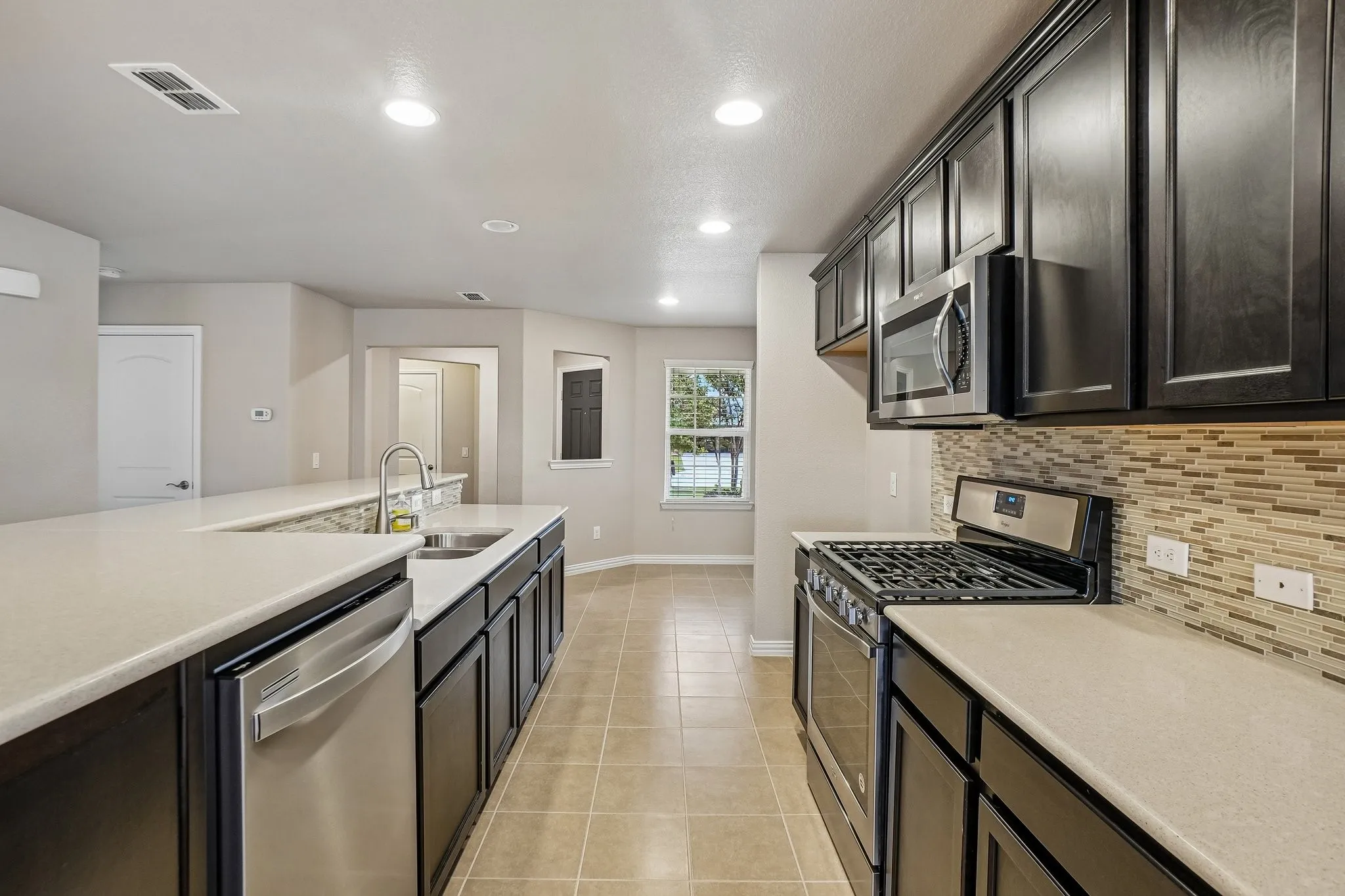 Kitchen featuring dark wood-finish cabinetry, light-toned countertops, stainless steel appliances, a mosaic tile backsplash, and recessed lighting
