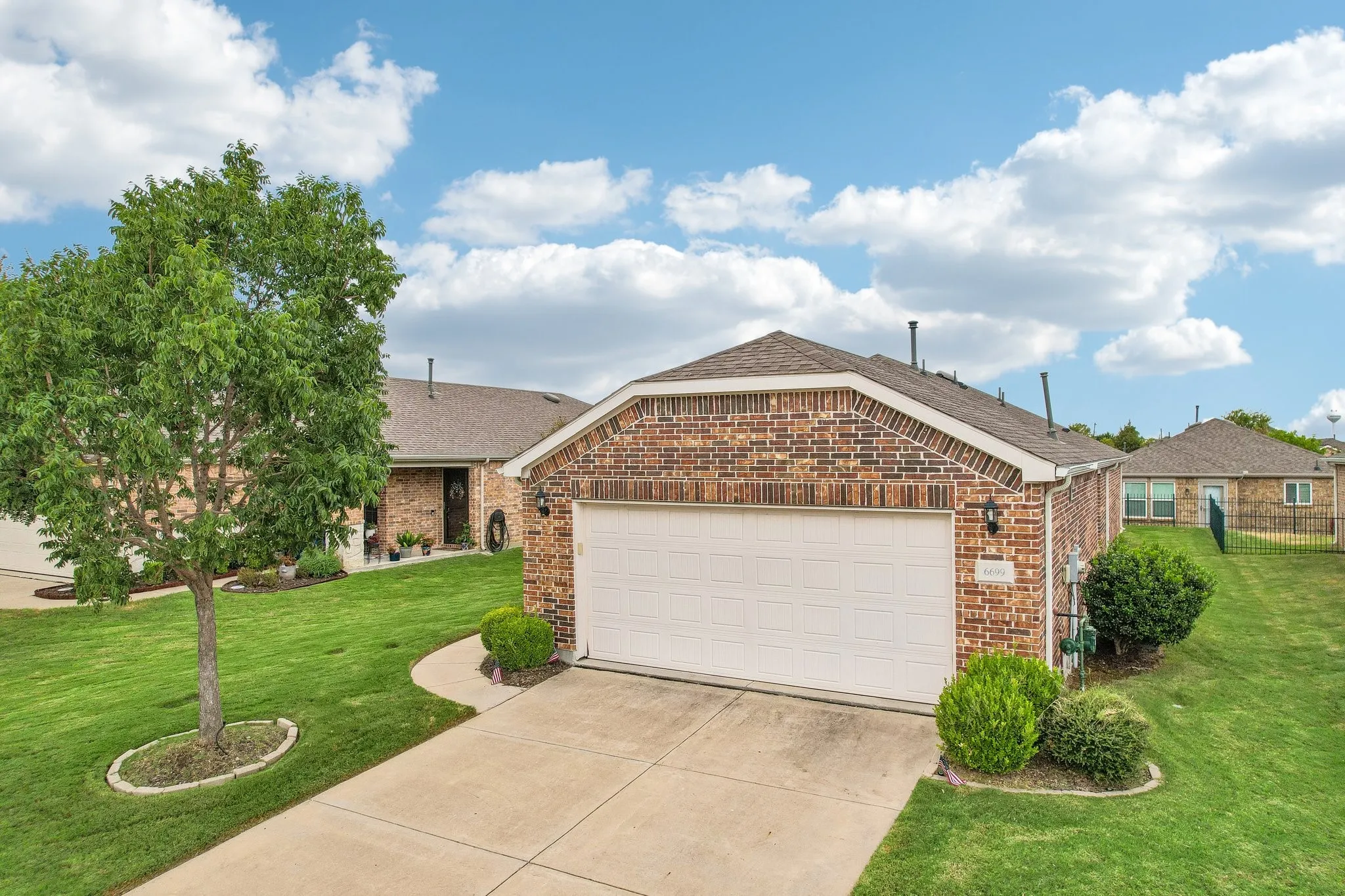 Brick exterior with an attached garage, concrete driveway, and mature landscaping