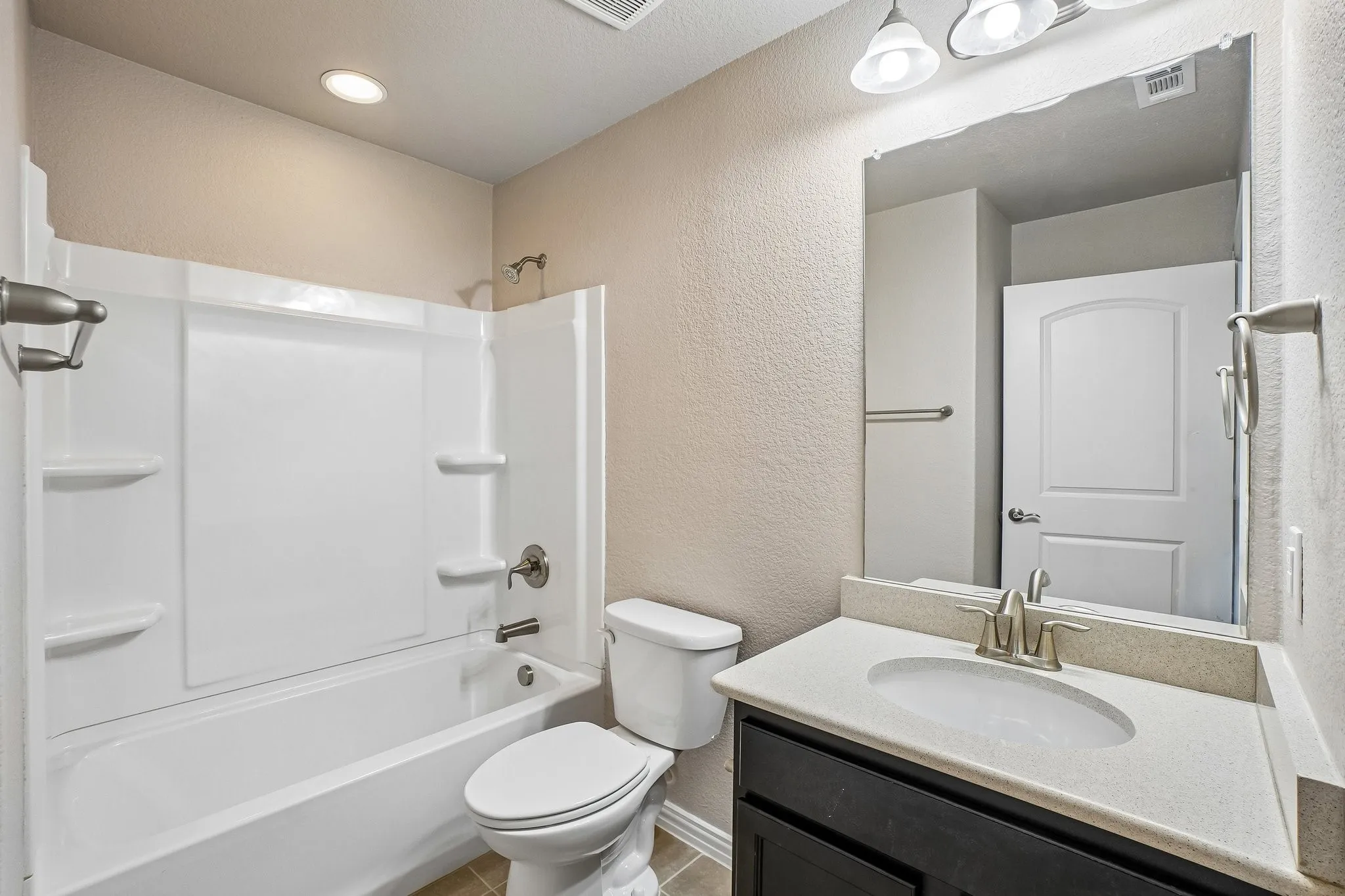 Bathroom featuring a white tub/shower combination, a vanity with a light-colored countertop, and a dark-finished cabinet