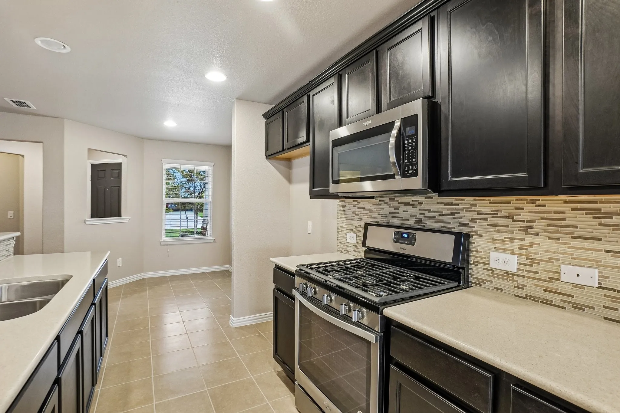 Kitchen featuring dark wood-finish cabinetry, stainless steel appliances, mosaic tile backsplash, and light-toned countertops