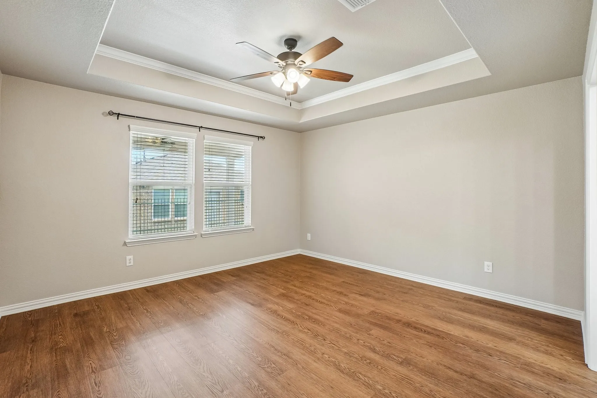Tray ceiling with crown molding, wood-finish flooring, two windows with blinds, and a ceiling fan with integrated lighting