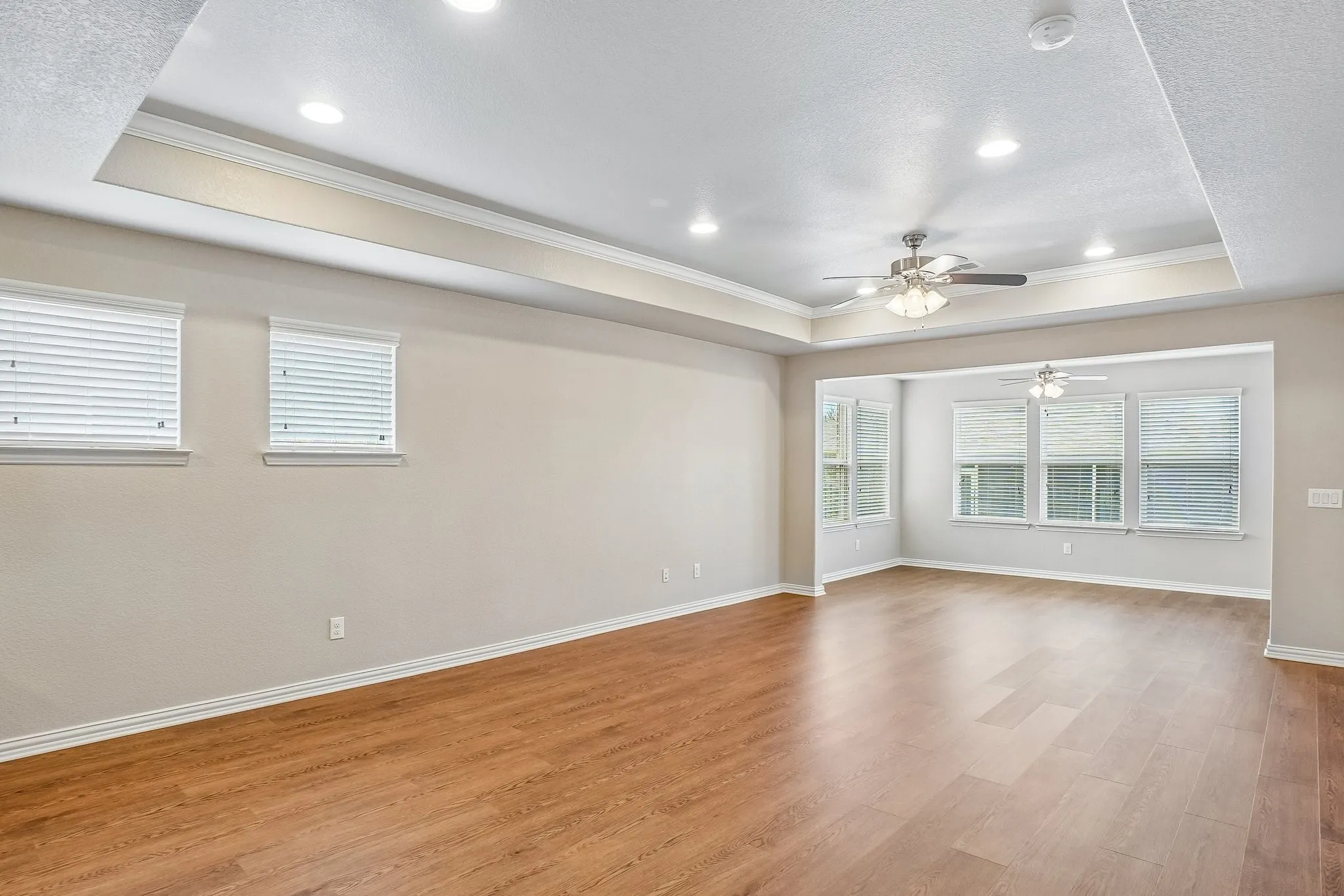 Wood-finish flooring throughout, tray ceiling with recessed lighting and a ceiling fan, and multiple windows with blinds