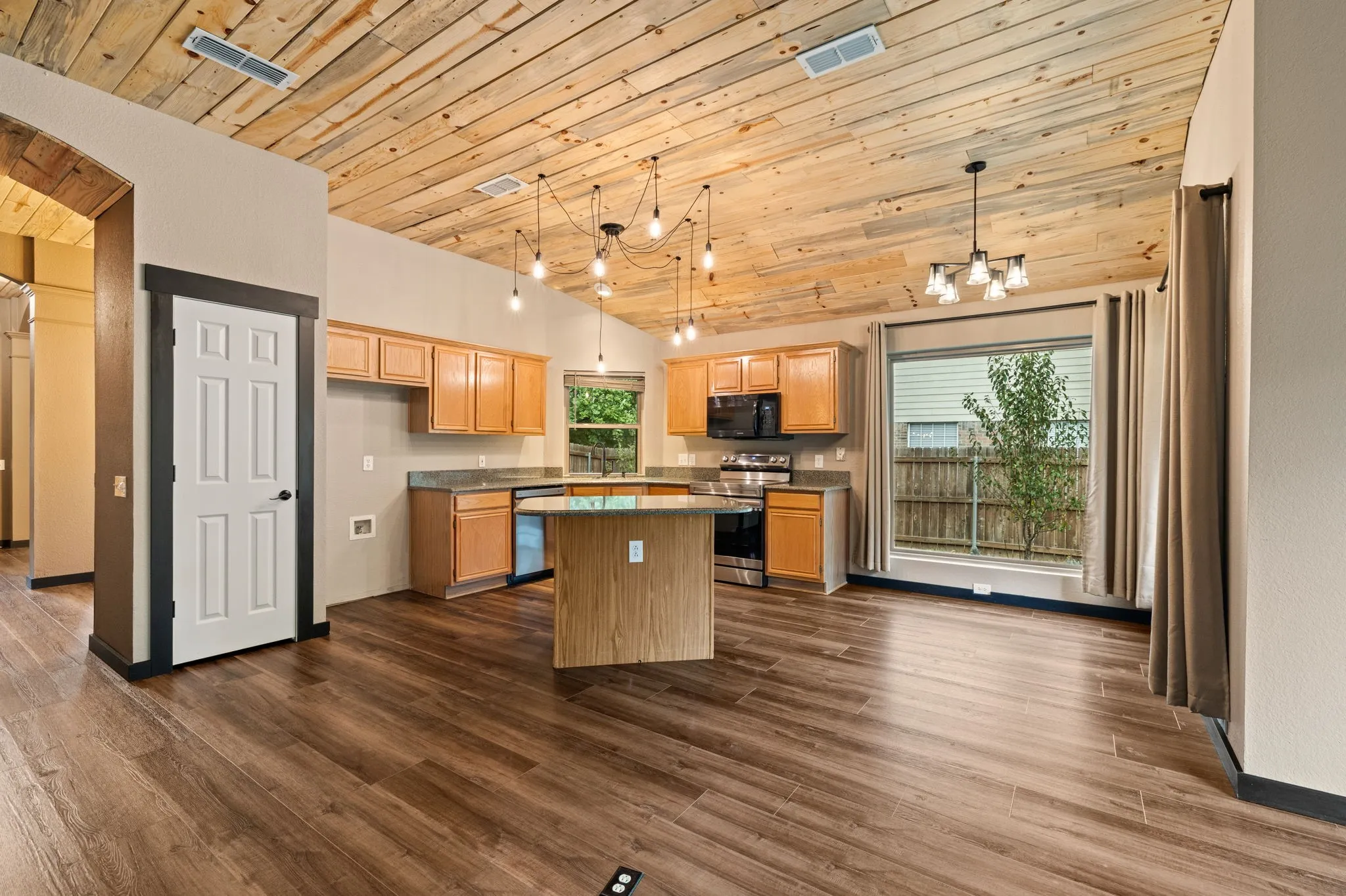 Vaulted wood-finish ceiling, wood-finish flooring, kitchen island with built-in storage, stainless steel appliances, and a large window