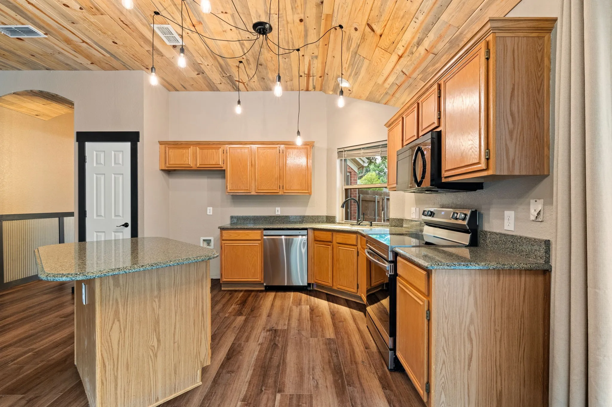 Vaulted wood-paneled ceiling, island with a stone-finish countertop, wood-finish flooring, wood cabinetry, and stainless steel appliances