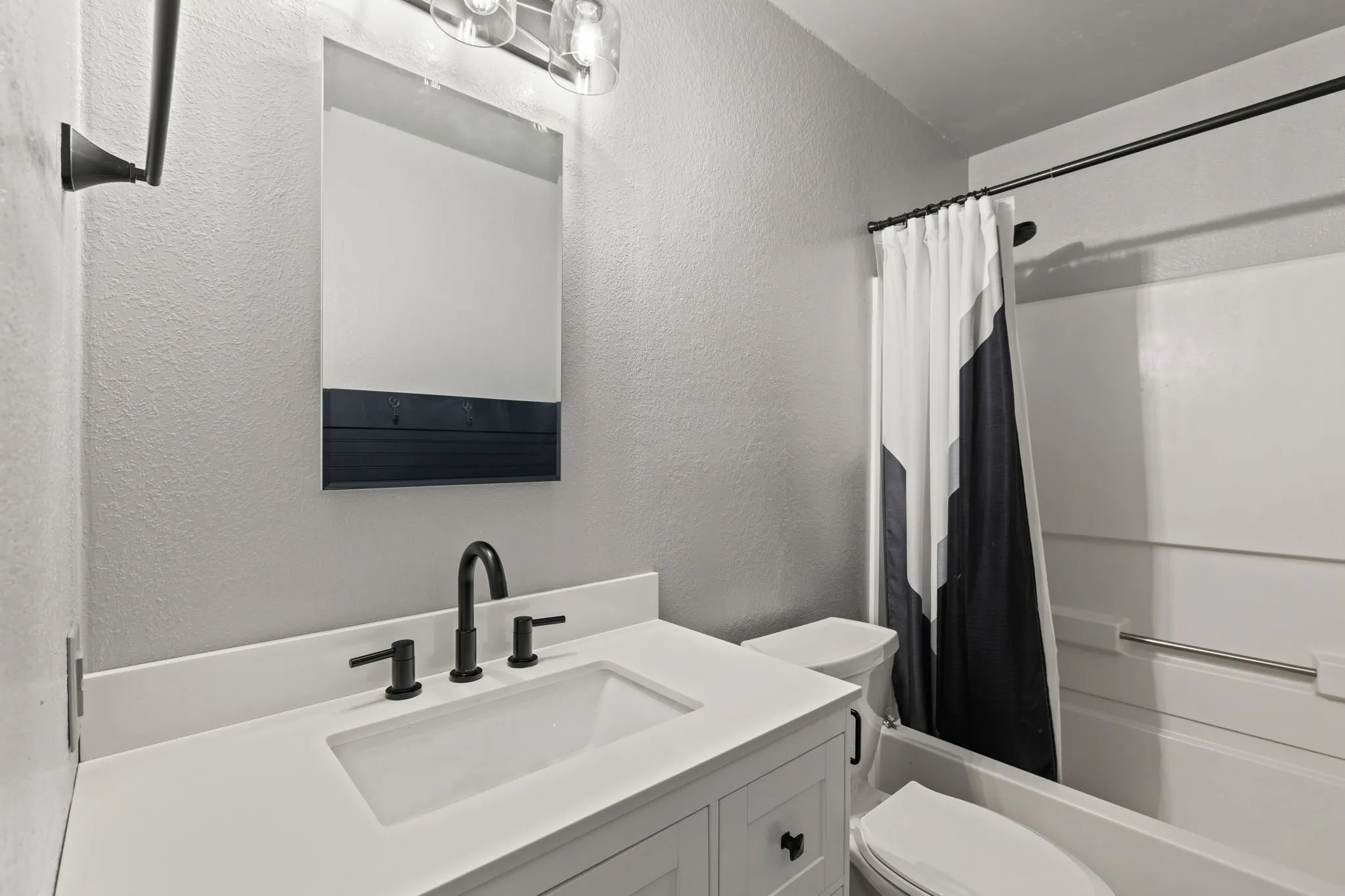 Vanity with a white countertop and integrated sink, matte black faucet, and a wall-mounted mirror