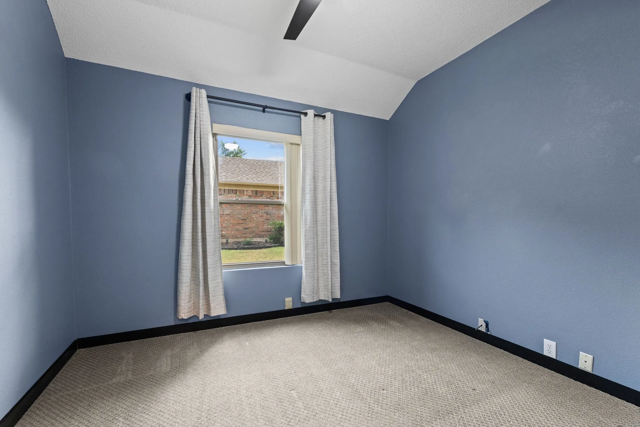 Vaulted ceiling with an integrated ceiling fan, window with window treatments, and carpeted flooring