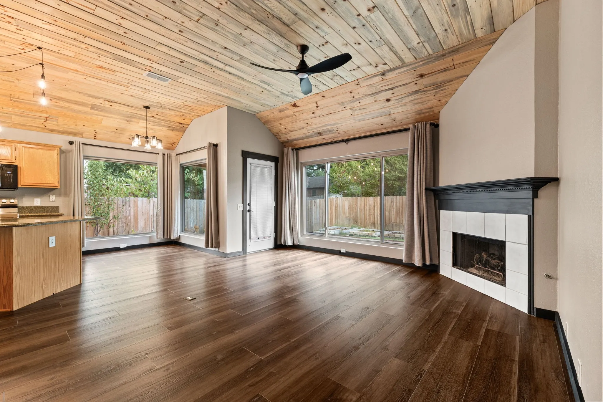 Wood-finish flooring throughout, vaulted plank wood-finish ceiling, built-in fireplace with white tile surround and dark mantel, and multiple windows