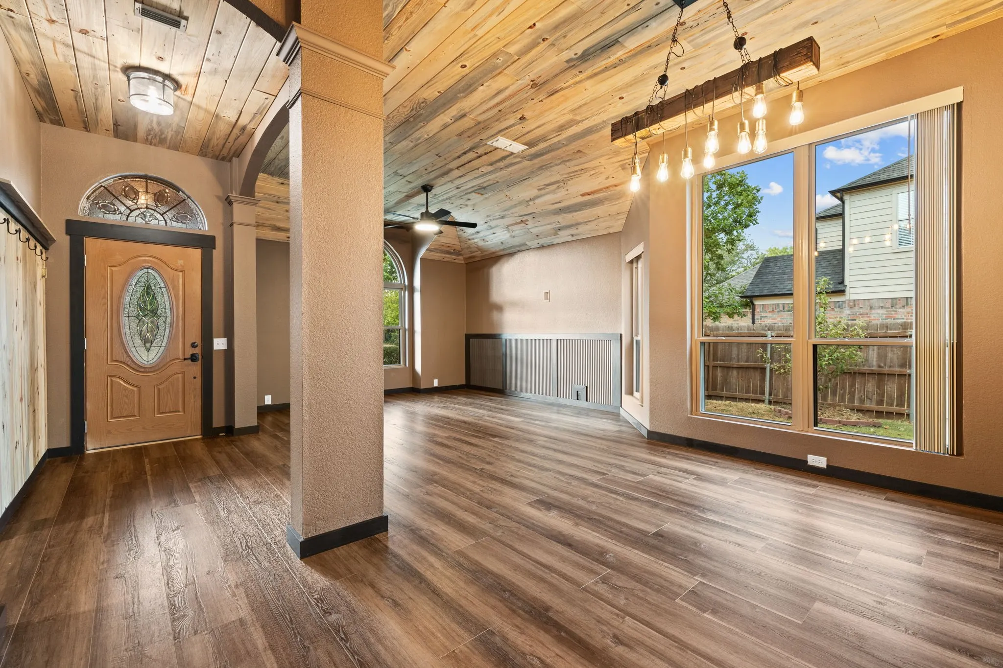 Vaulted wood-finish ceiling, wood-finish flooring, full-light entry door with decorative glass, decorative ceiling fan, and extensive windows