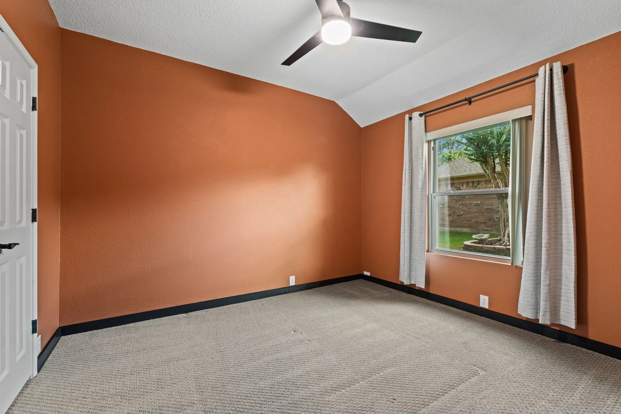Vaulted ceiling with an attached ceiling fan, carpeted flooring, and a window with roller shades