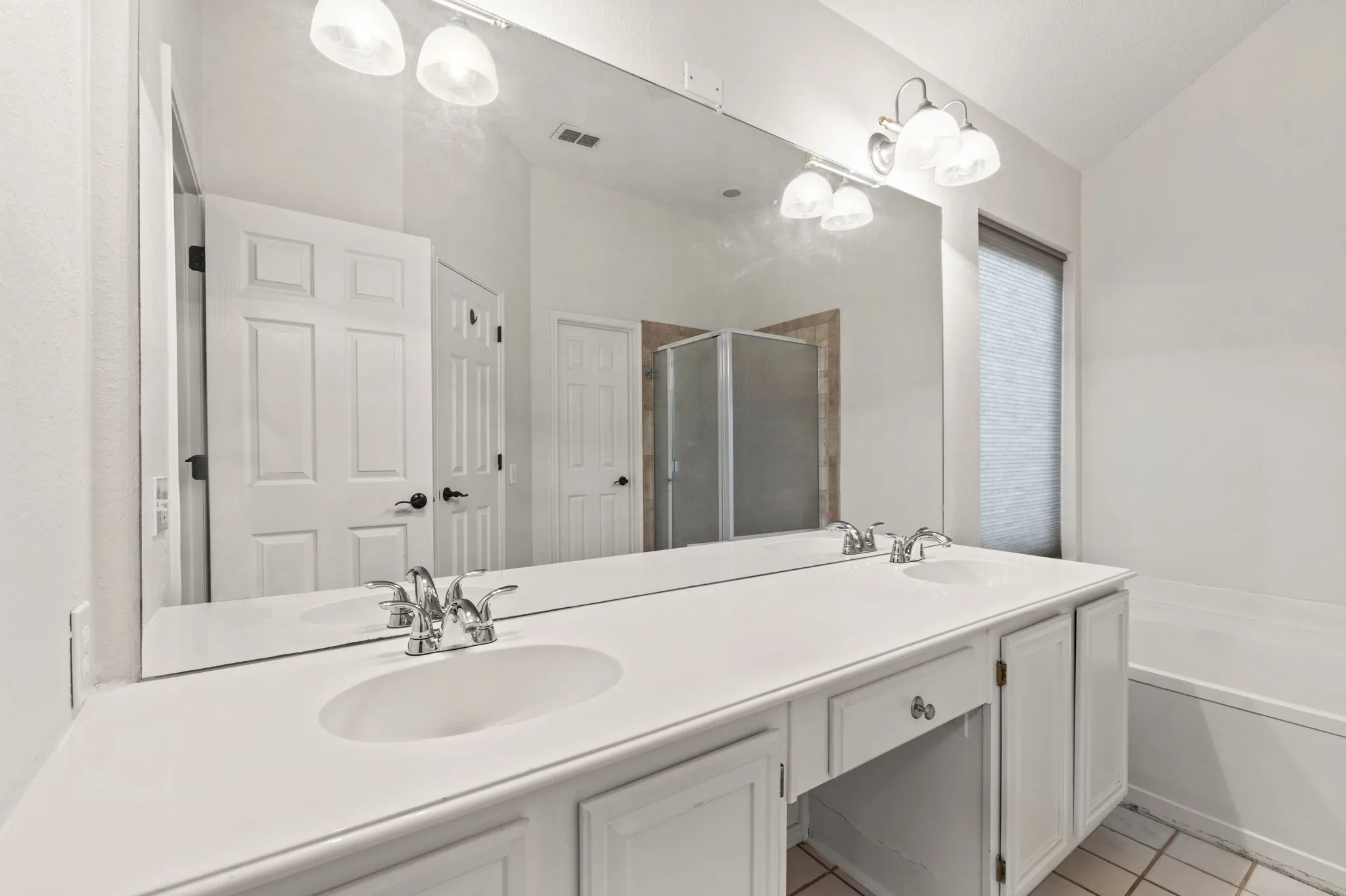 Dual undermount sinks with chrome fixtures, expansive countertop vanity with built-in cabinetry, and a full-width wall-mounted mirror
