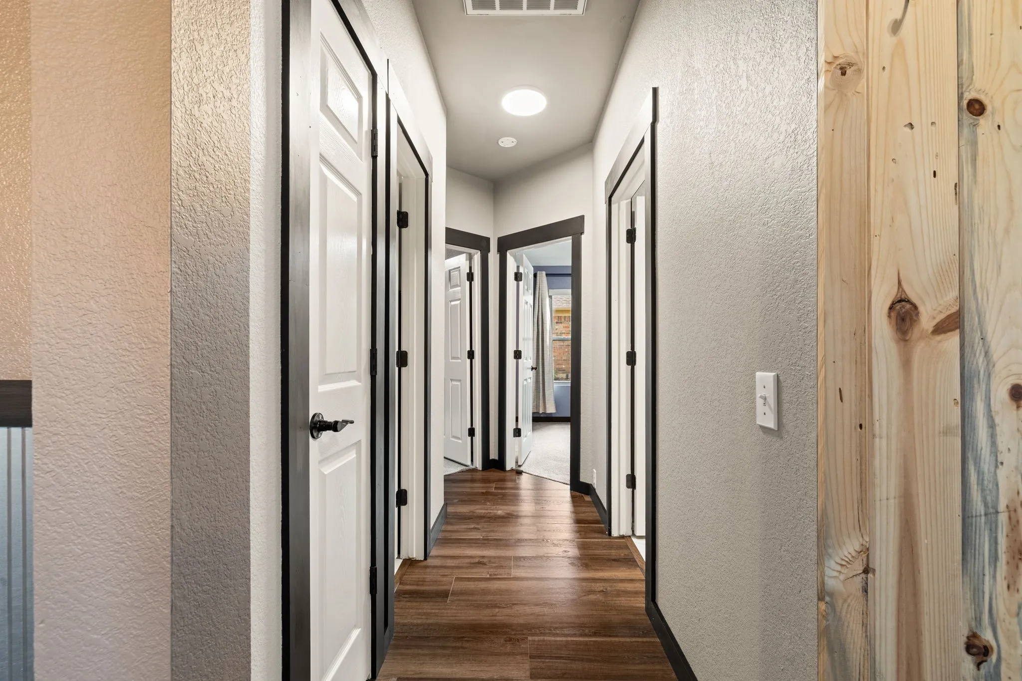 Hallway featuring wood-finish flooring, white paneled doors with dark trim, recessed ceiling lighting, and a prominent wood-paneled wall accent