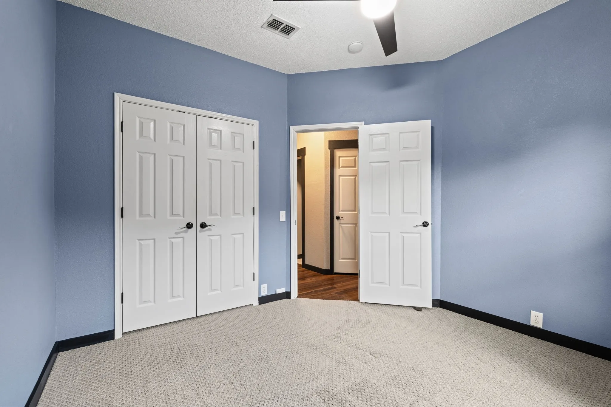 White paneled doors, carpeted flooring, and a ceiling fan with integrated lighting