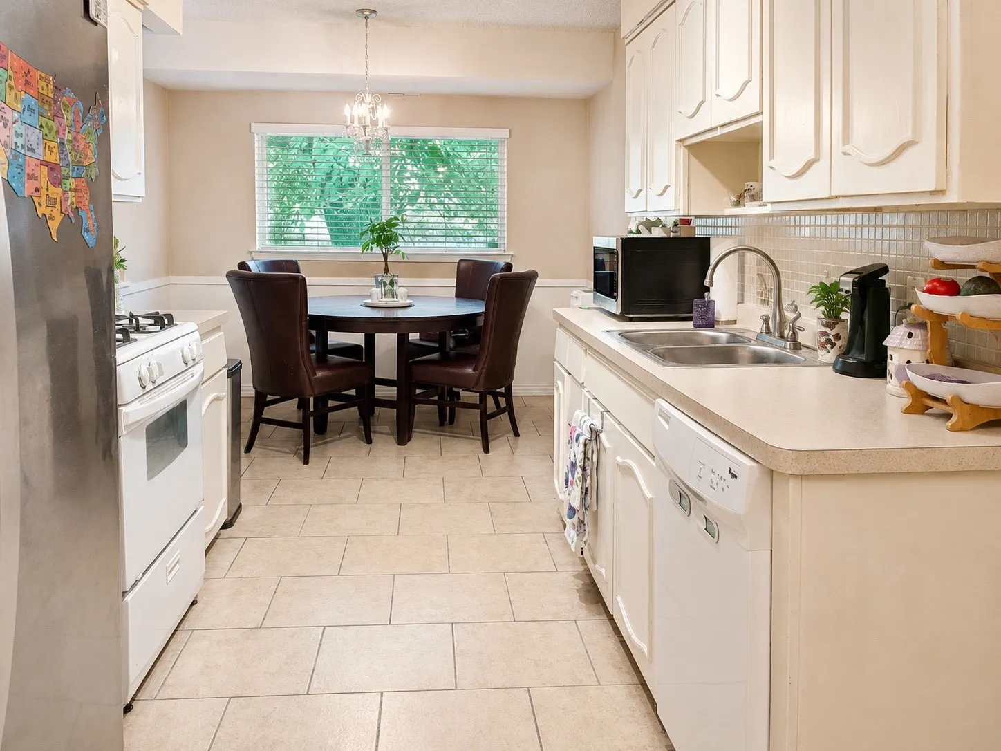 Bright, galley-style kitchen featuring cream cabinetry with raised-panel doors, tile countertops, stainless steel appliances, and a ceramic tile floor