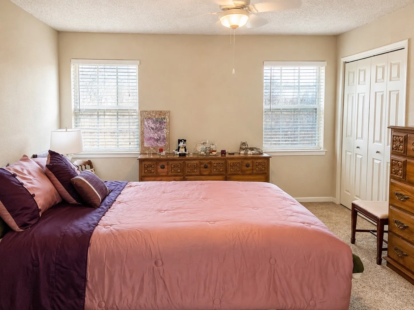 Neutral tone walls, ceiling fan with light fixture, carpeted flooring, two windows with blinds, and bi-fold closet doors